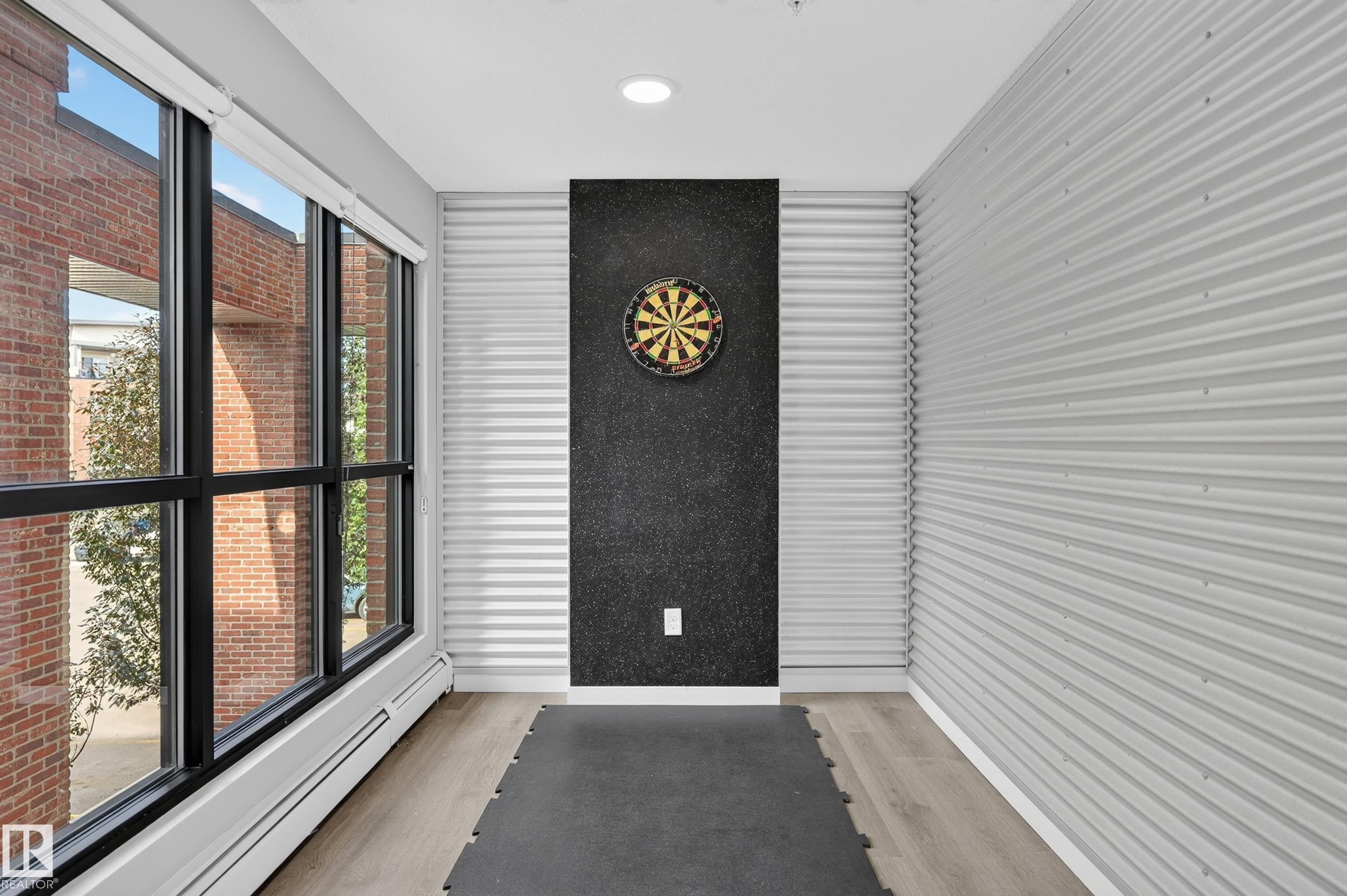 Full-height windows with black framing, wood-finish flooring, recessed ceiling lighting, and textured wall paneling - #131 5504 Schonsee Dr Nw, Edmonton, AB - Indoor Photo Showing Other Room