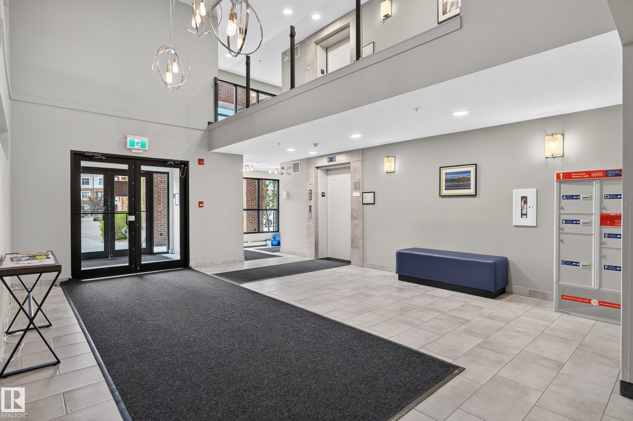 Two-story lobby featuring ceramic tile flooring, modern pendant lighting, and an elevator - #131 5504 Schonsee Dr Nw, Edmonton, AB - Indoor Photo Showing Other Room