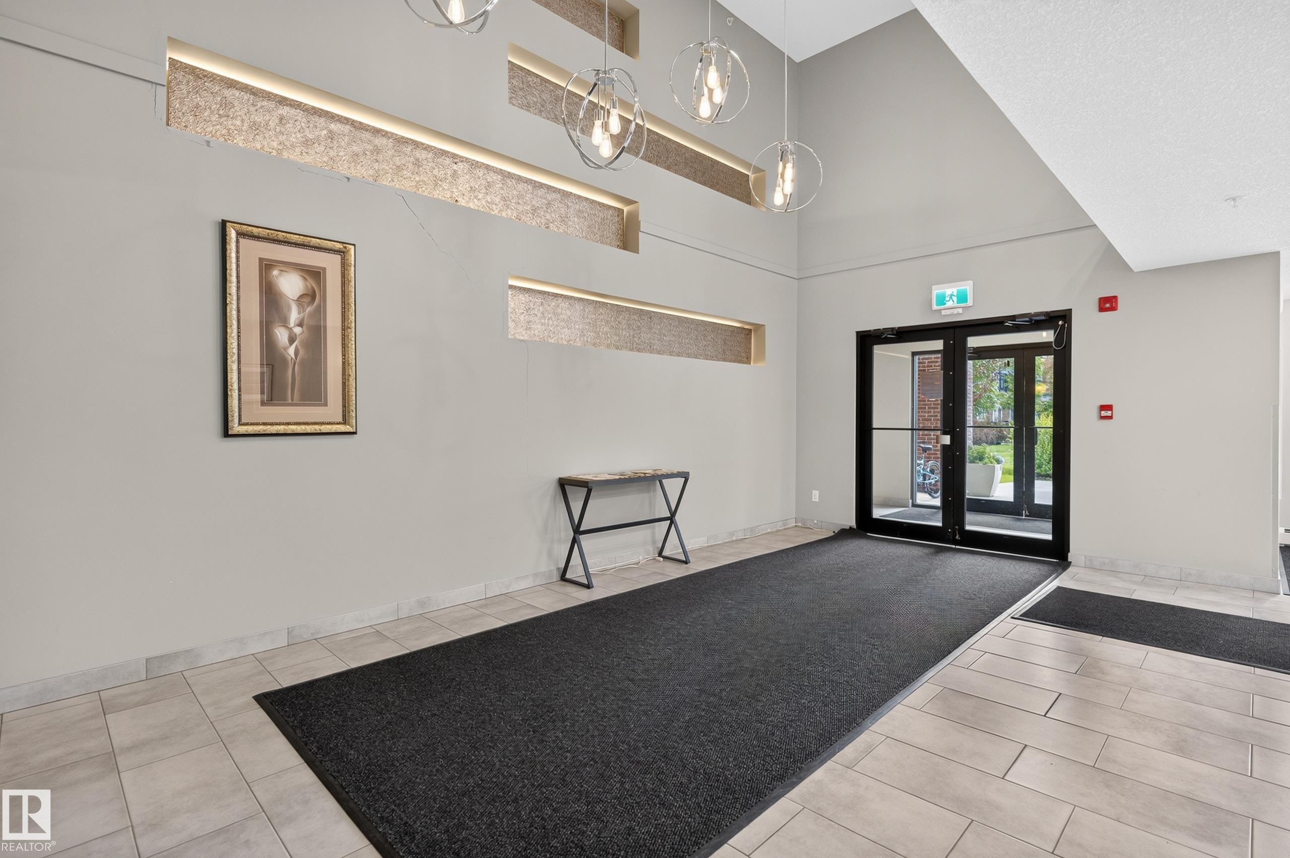 Lobby entrance featuring double glass doors, tile flooring, and decorative wall cutouts with integrated lighting - #131 5504 Schonsee Dr Nw, Edmonton, AB - Indoor Photo Showing Other Room
