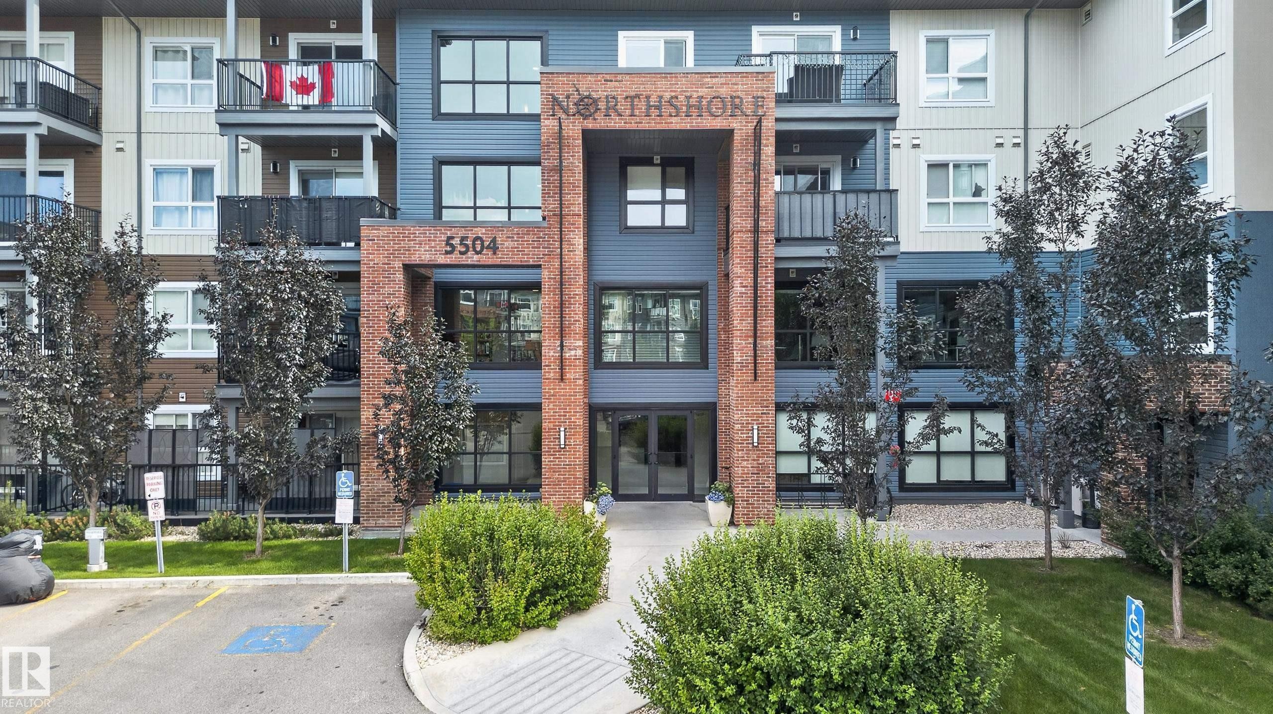 Multi-story building featuring a brick and siding facade, multiple balconies with black railings, and a prominent entrance - #131 5504 Schonsee Dr Nw, Edmonton, AB - Outdoor With Balcony With Facade