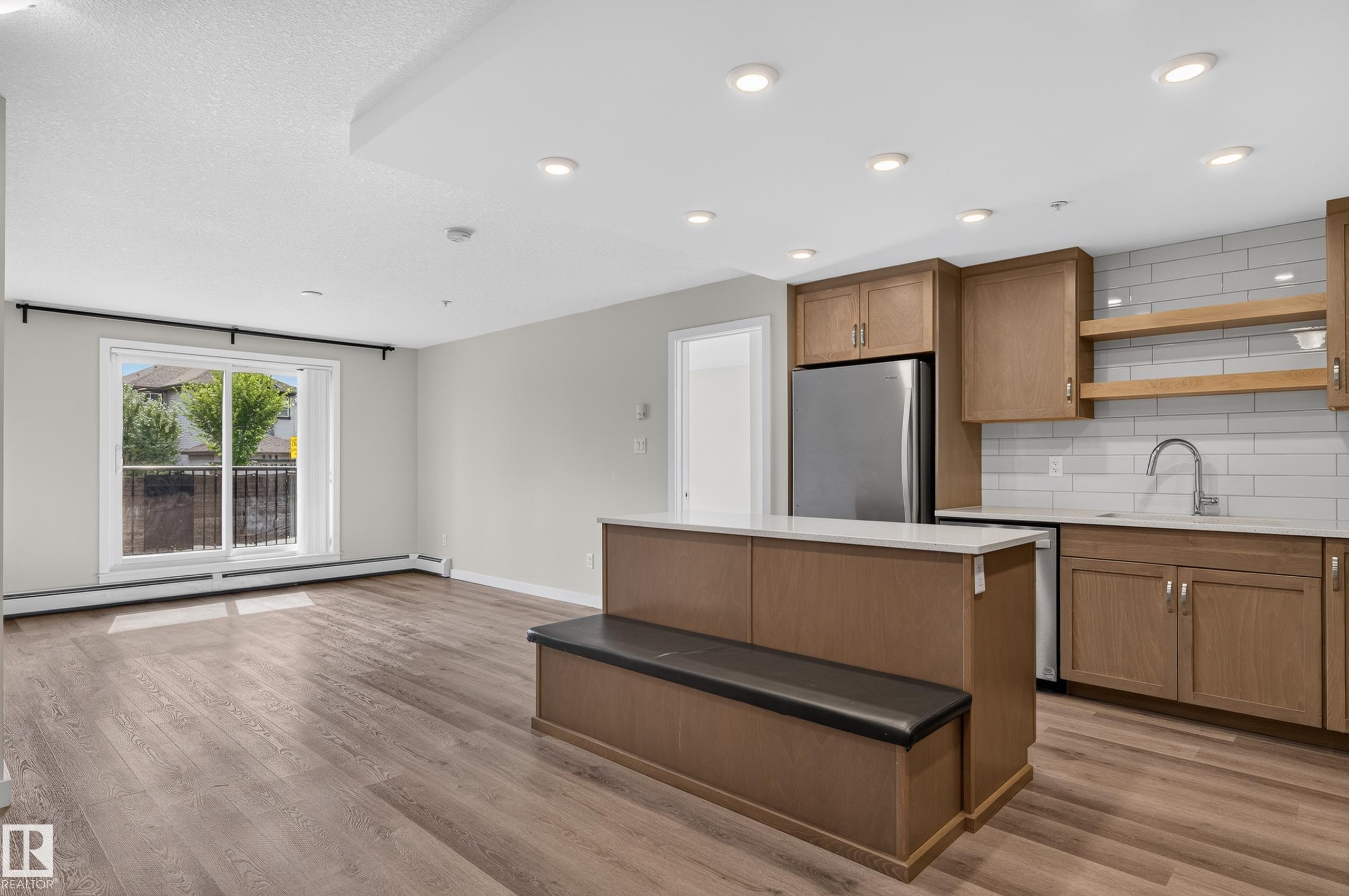Open-concept living space featuring wood-finish flooring, recessed lighting, and a sliding glass door - #131 5504 Schonsee Dr Nw, Edmonton, AB - Indoor Photo Showing Kitchen
