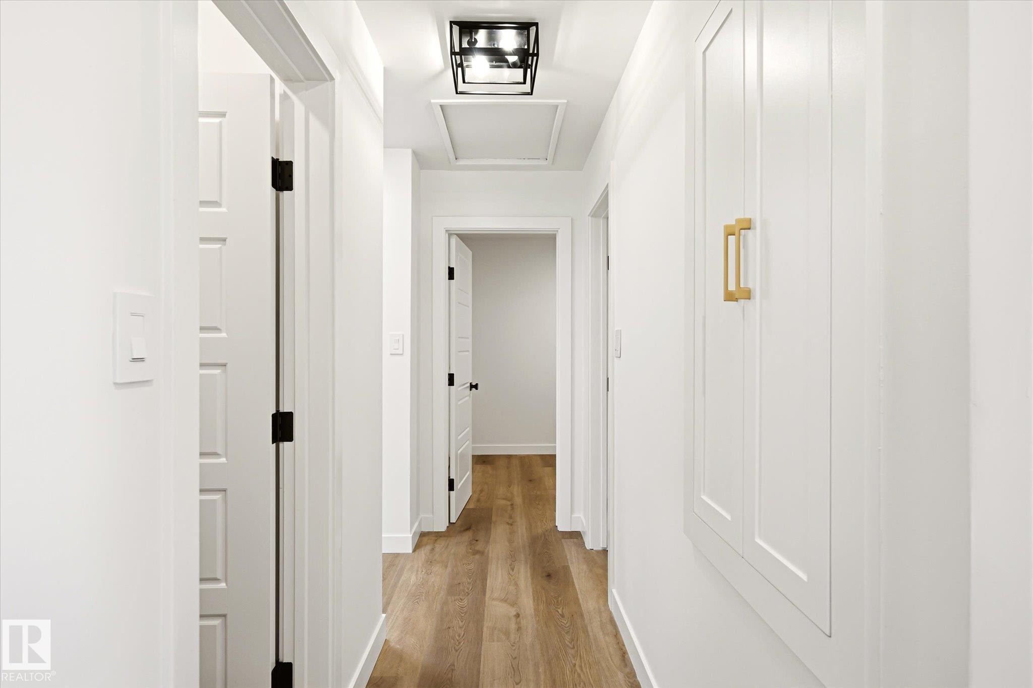 Clean hallway featuring wood-finish flooring, white paneled doors with matte black hardware, and a modern ceiling light fixture - 4708 104A Avenue Nw, Edmonton, AB - Indoor Photo Showing Other Room