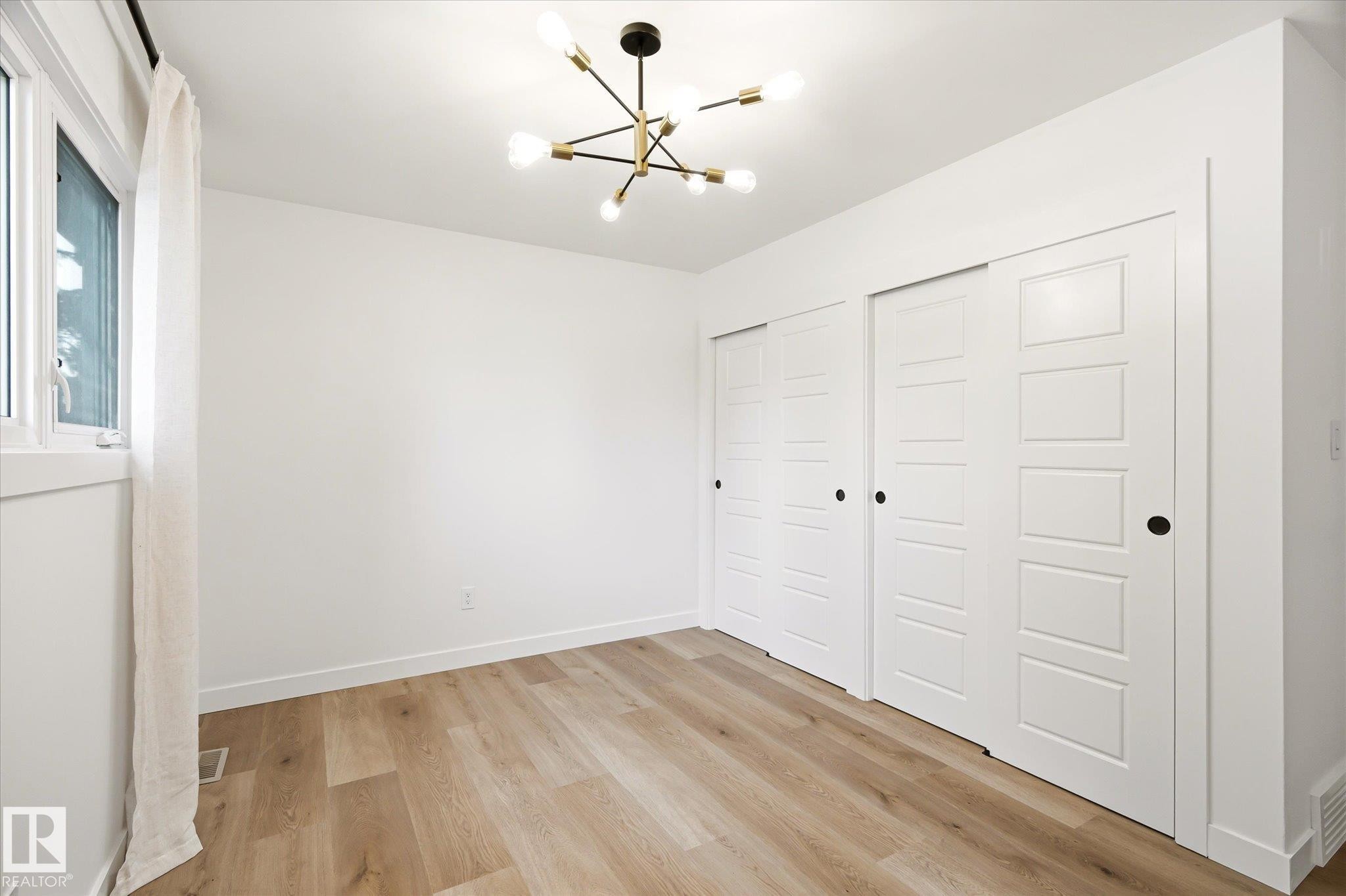 Room featuring wood-finish flooring, a contemporary chandelier, white walls, and a window - 4708 104A Avenue Nw, Edmonton, AB - Indoor Photo Showing Other Room