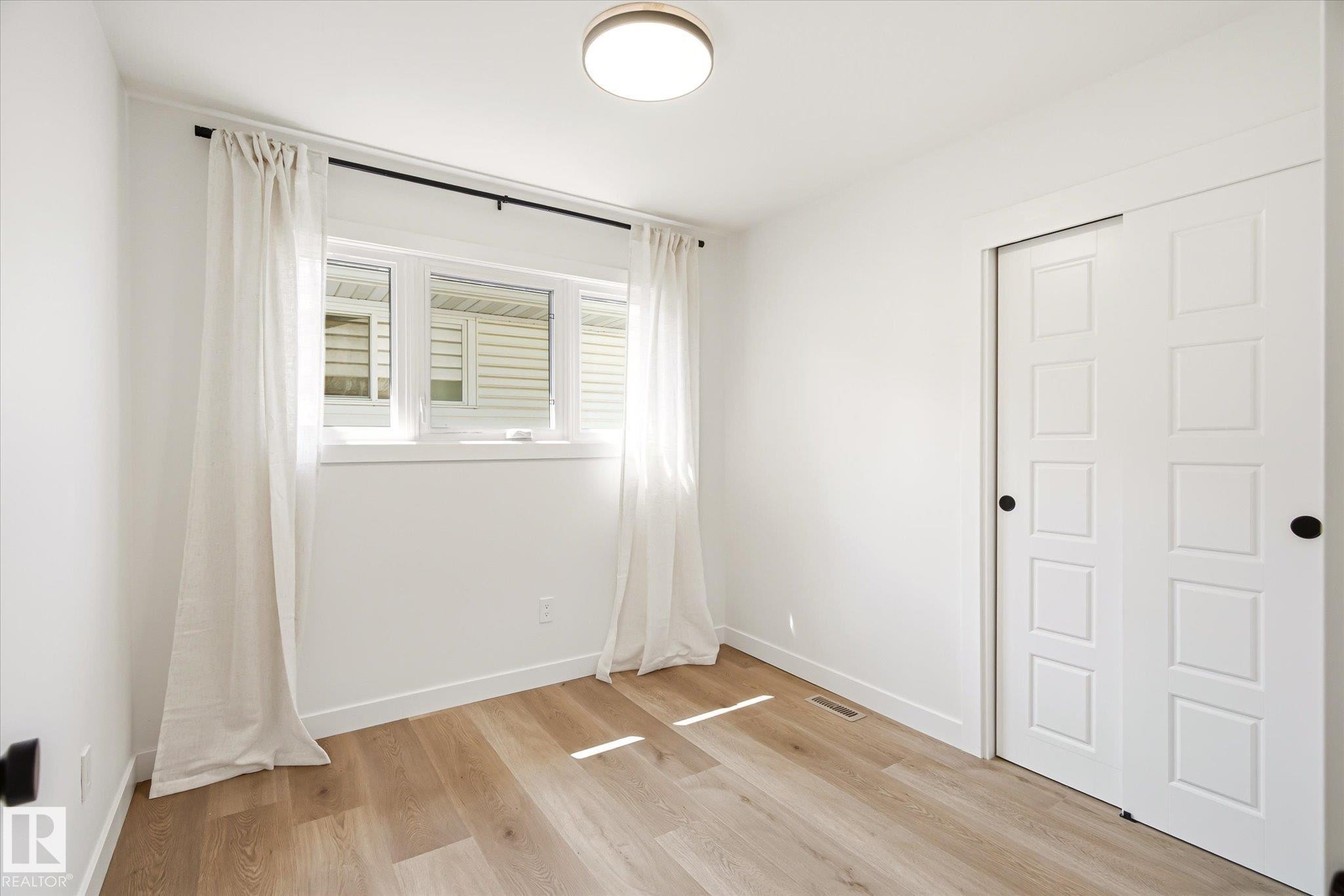 Bright interior space featuring a window with white trim, wood-finish flooring, and a flush mount ceiling light - 4708 104A Avenue Nw, Edmonton, AB - Indoor Photo Showing Other Room
