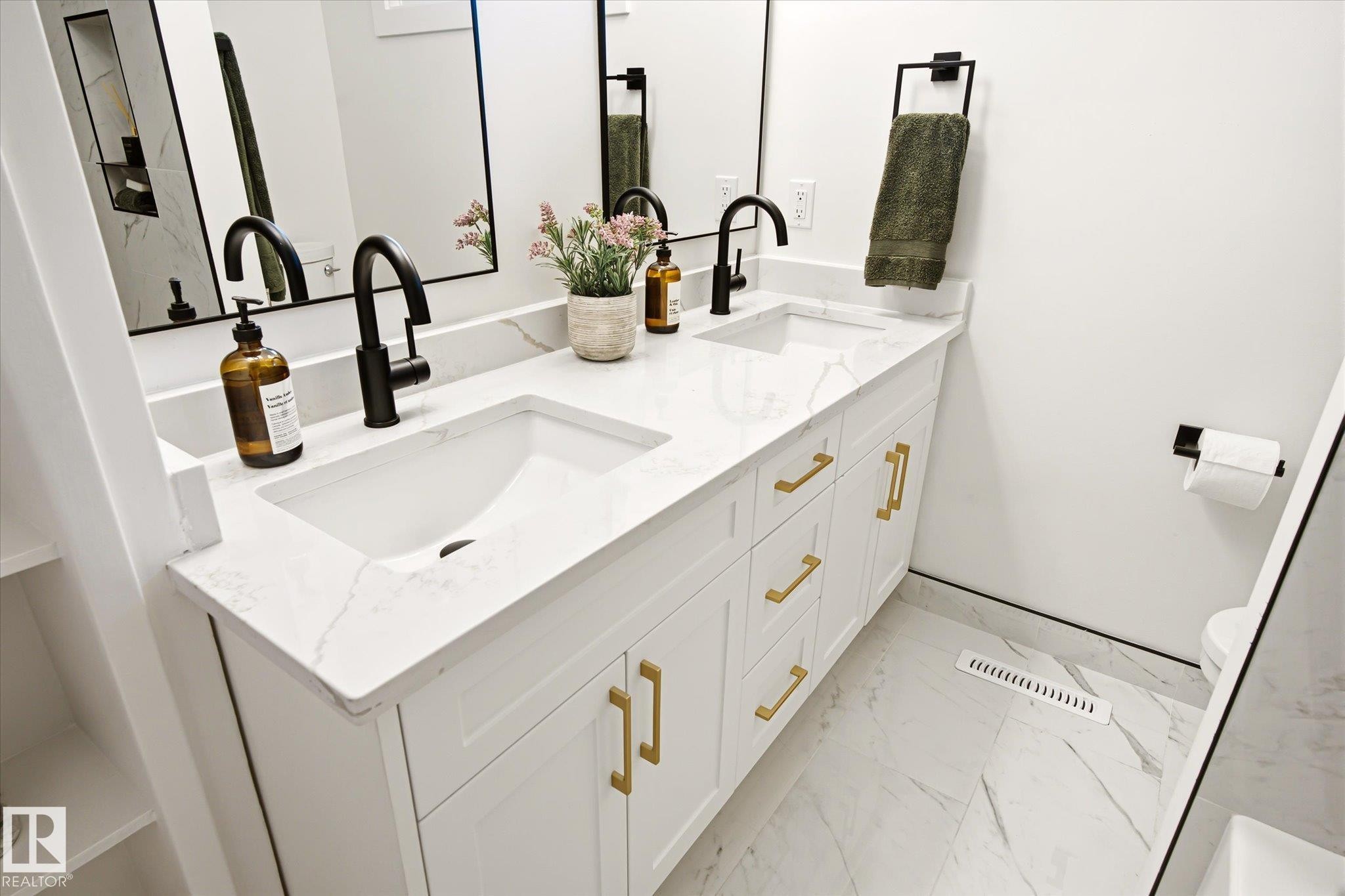 Dual vanity with integrated sinks, white cabinetry, gold-finish hardware, black-finish faucets, and patterned flooring - 4708 104A Avenue Nw, Edmonton, AB - Indoor Photo Showing Bathroom