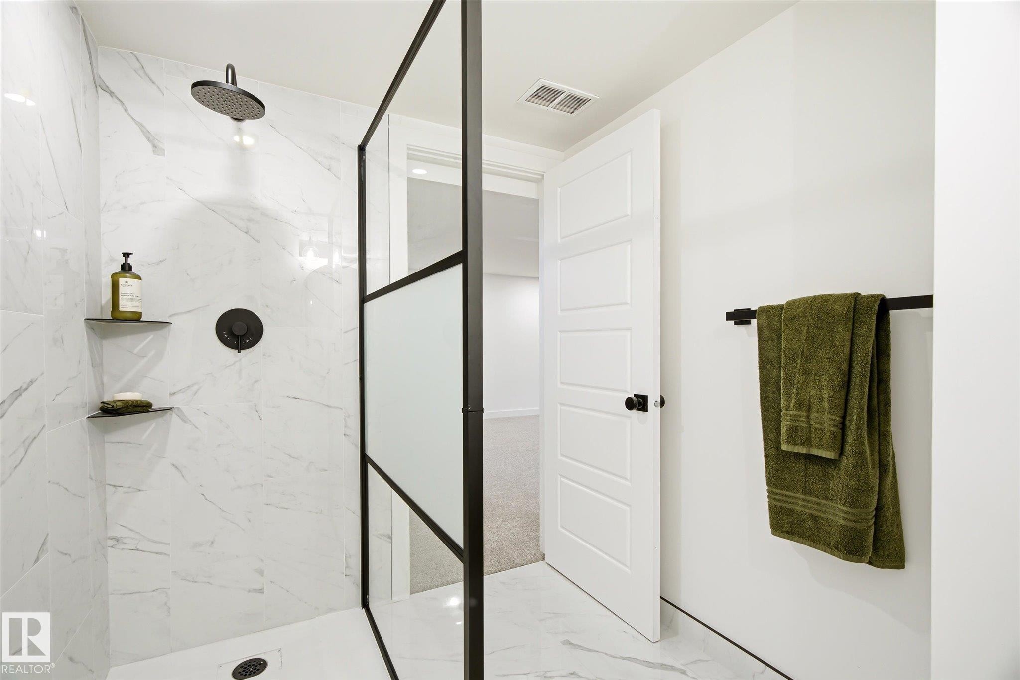 Walk-in shower featuring a grid-patterned glass partition, white marbled tile, a matte black rain showerhead, and built-in shelving - 4708 104A Avenue Nw, Edmonton, AB - Indoor