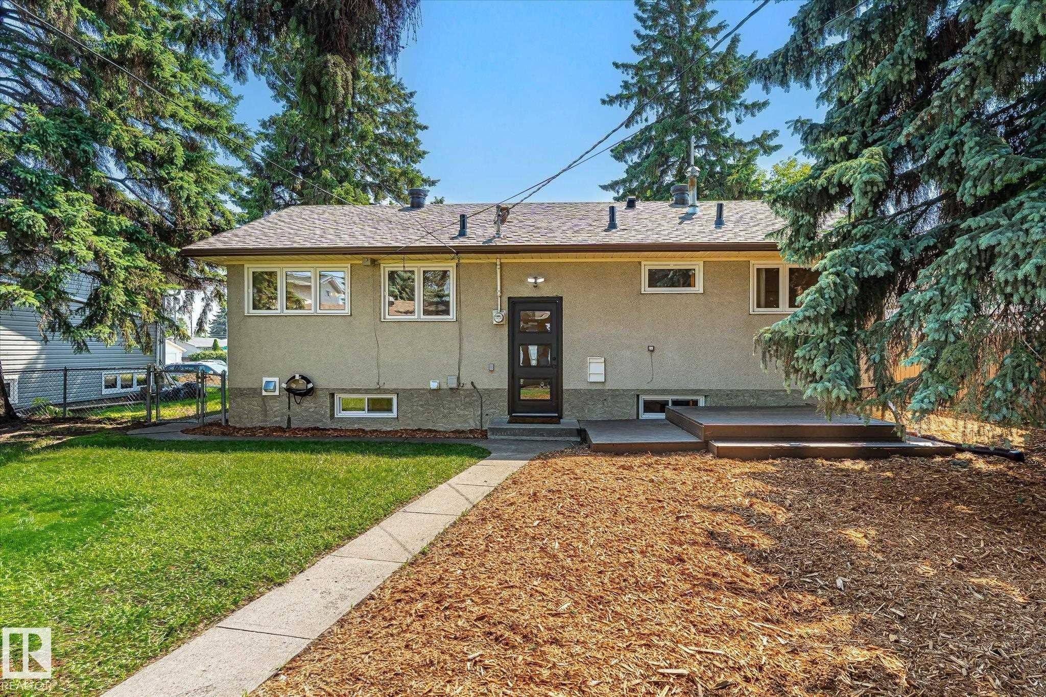 Rear exterior featuring an elevated multi-level deck, concrete walkway, and a mix of lawn and wood mulch landscaping - 4708 104A Avenue Nw, Edmonton, AB - Outdoor