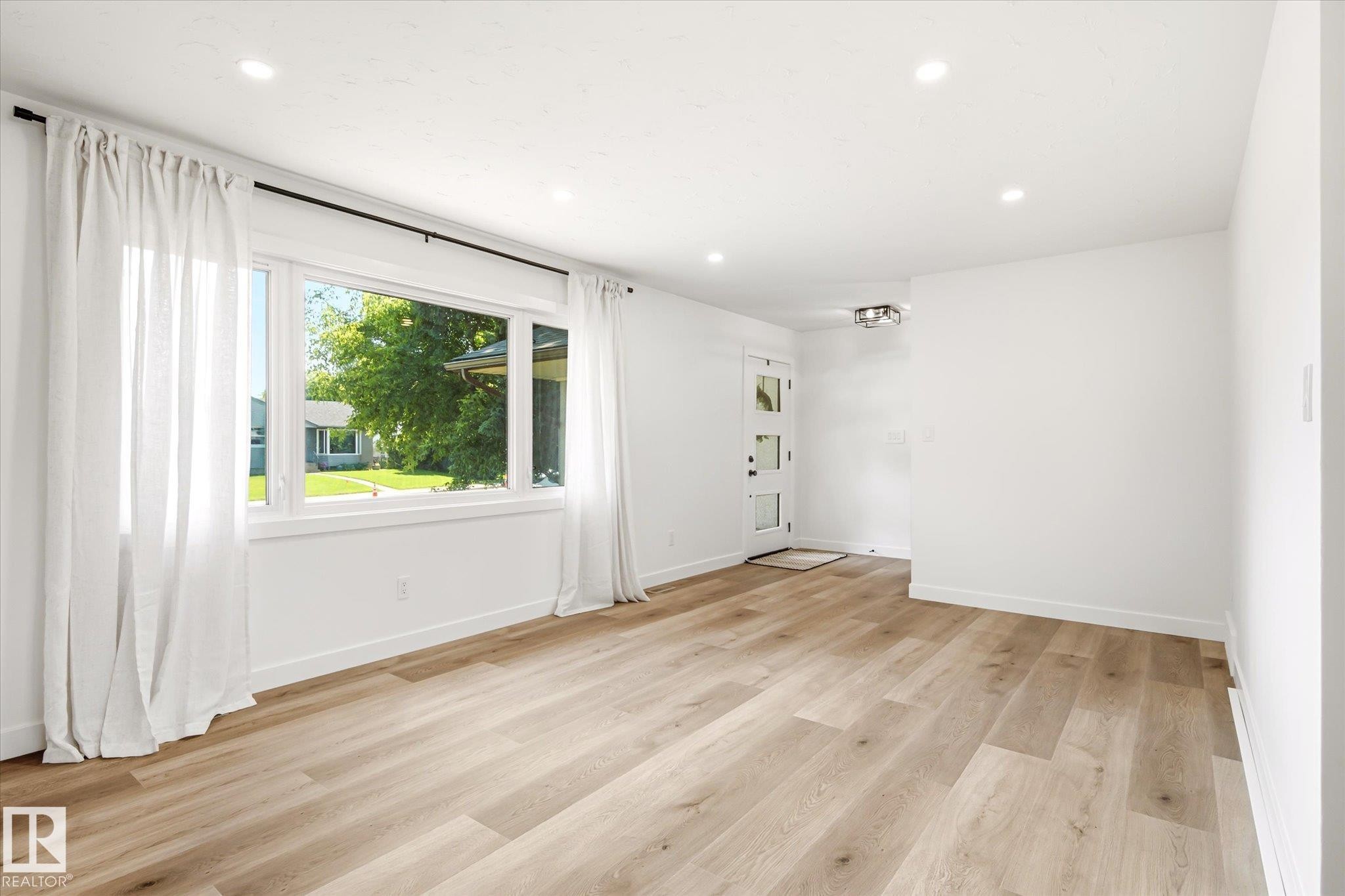 Open-concept living area featuring wood-finish flooring, recessed lighting, and a white paneled entry door with frosted glass inserts - 4708 104A Avenue Nw, Edmonton, AB - Indoor Photo Showing Other Room