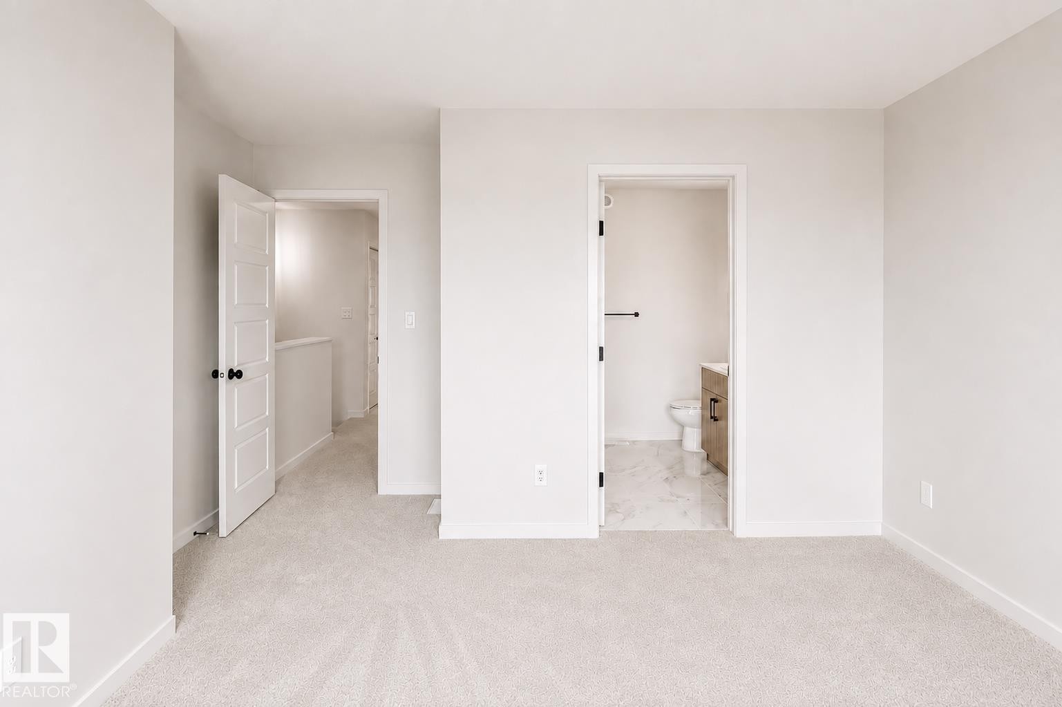 Plush carpeting, a paneled interior door, and a full bathroom with marble-finish flooring and a wood-finish vanity - 219 157 Avenue Ne, Edmonton, AB - Indoor Photo Showing Other Room