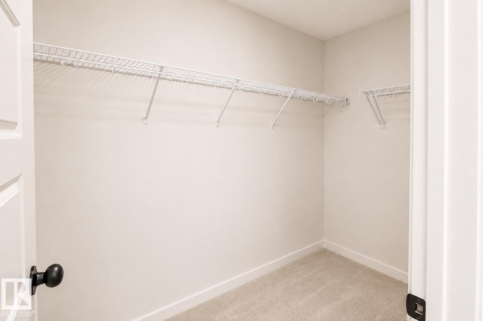 Built-in wire shelving system, light neutral wall color, light neutral carpet, white trim, and a white panel door with black hardware - 219 157 Avenue Ne, Edmonton, AB - Indoor With Storage