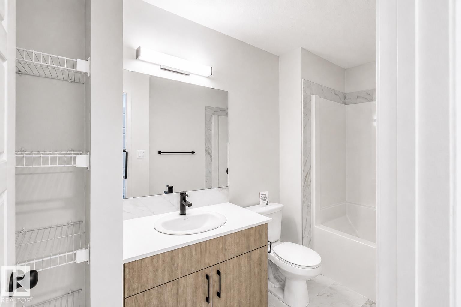 Full bathroom featuring a single vanity with wood-finish cabinetry, a rectangular undermount sink, and a white countertop - 219 157 Avenue Ne, Edmonton, AB - Indoor Photo Showing Bathroom