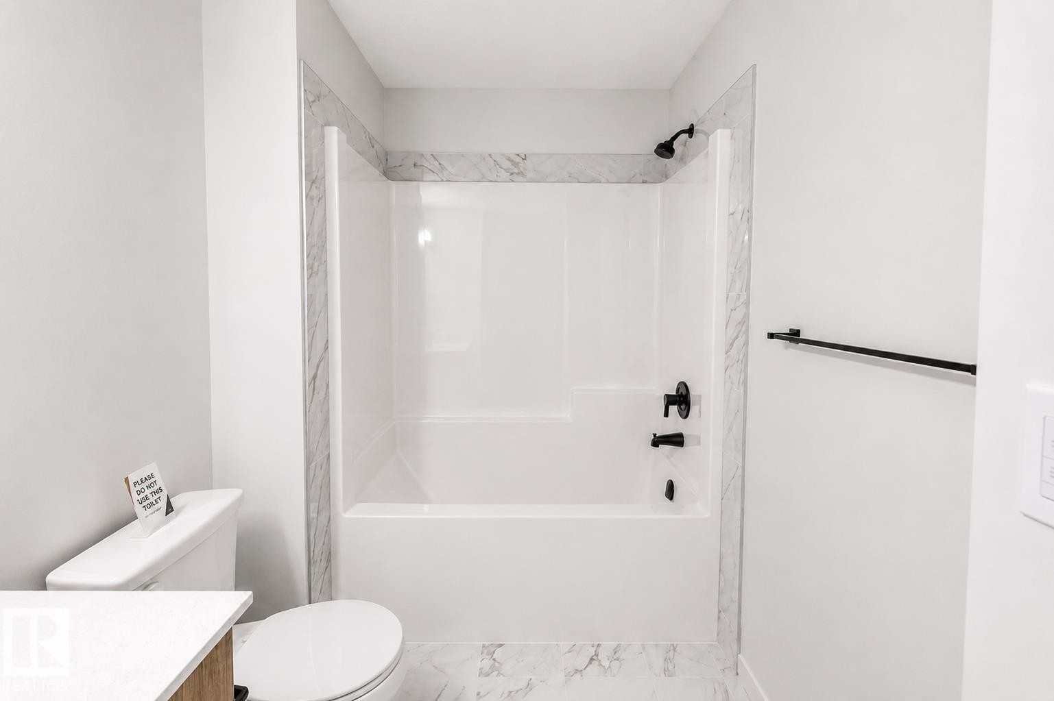 Bathtub and shower combination with matte black fixtures, framed by marble-look tile surround and complementing floor tile - 219 157 Avenue Ne, Edmonton, AB - Indoor Photo Showing Bathroom