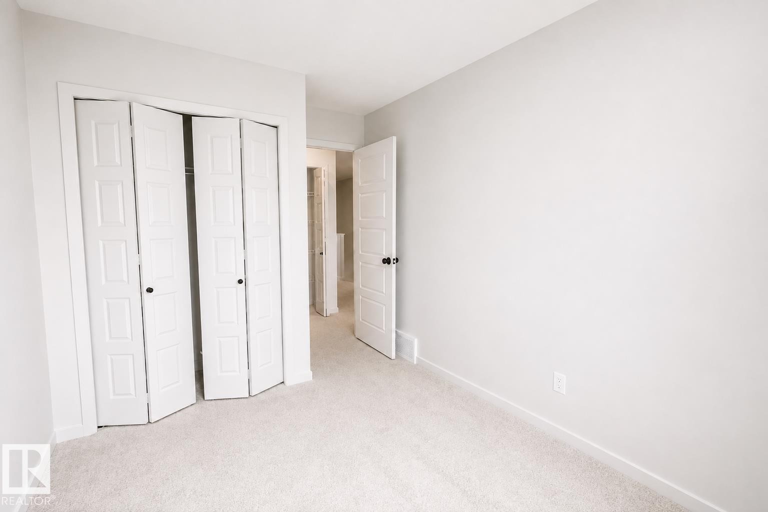 Light-colored carpeting, white walls, and white bi-fold closet doors with black hardware - 219 157 Avenue Ne, Edmonton, AB - Indoor Photo Showing Other Room