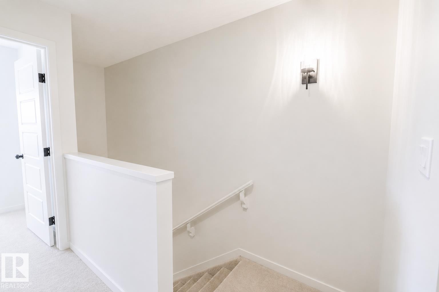 Carpeted hallway with a panel door, black hardware, and a wall-mounted light fixture - 219 157 Avenue Ne, Edmonton, AB - Indoor