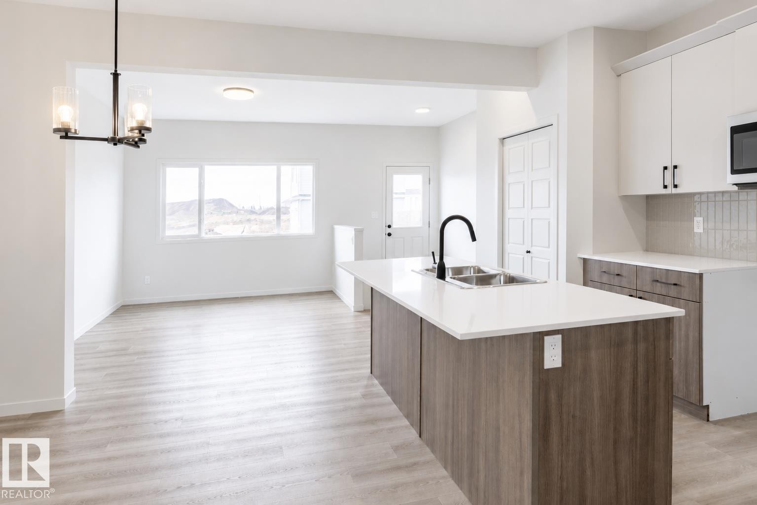 Open-concept kitchen with wood-finish flooring, a central island featuring a double-basin sink and matte black faucet, white shaker-style upper cabinetry, and a subway tile backsplash - 219 157 Avenue Ne, Edmonton, AB - Indoor Photo Showing Kitchen With Double Sink With Upgraded Kitchen