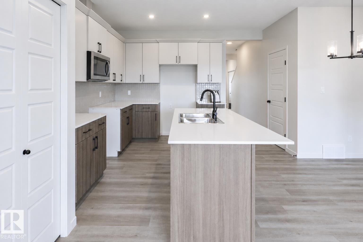 Kitchen featuring wood-finish flooring, white countertops, two-tone cabinetry, stainless steel microwave, and a center island with sink - 219 157 Avenue Ne, Edmonton, AB - Indoor Photo Showing Kitchen With Double Sink
