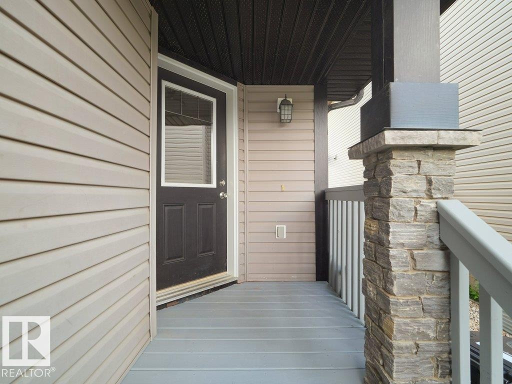 Covered entry featuring plank flooring, a detailed stone column, a dark wood-finish door with upper window, and horizontal siding - 3010 17A Ave Nw, Edmonton, AB - Outdoor With Exterior