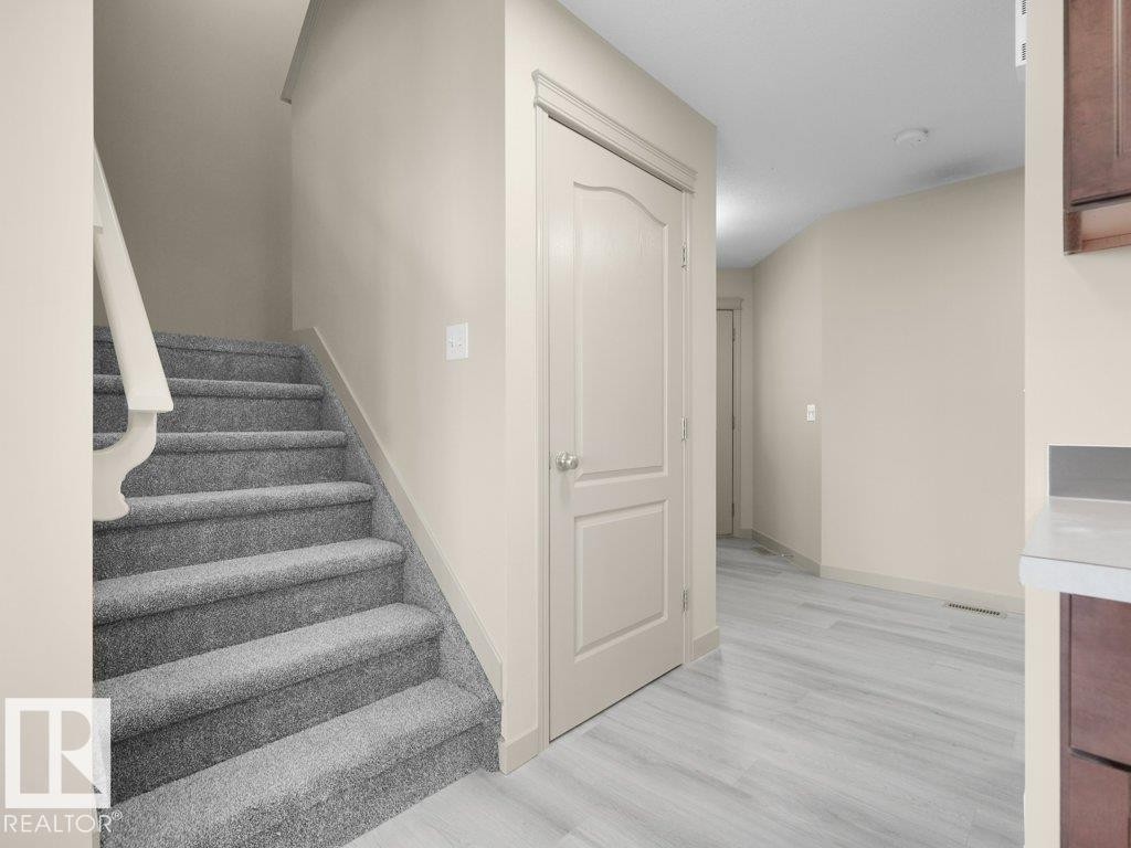 Carpeted staircase with painted handrail, solid interior doors, light wood-finish flooring, and light-toned walls - 3010 17A Ave Nw, Edmonton, AB - Indoor Photo Showing Other Room
