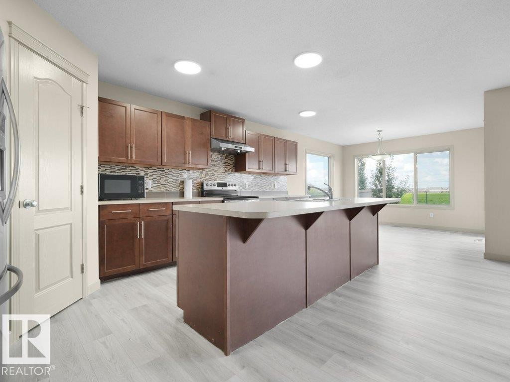 Open-concept kitchen with wood-finish flooring, recessed lighting, expansive windows, and a central island with integrated seating - 3010 17A Ave Nw, Edmonton, AB - Indoor Photo Showing Kitchen With Upgraded Kitchen