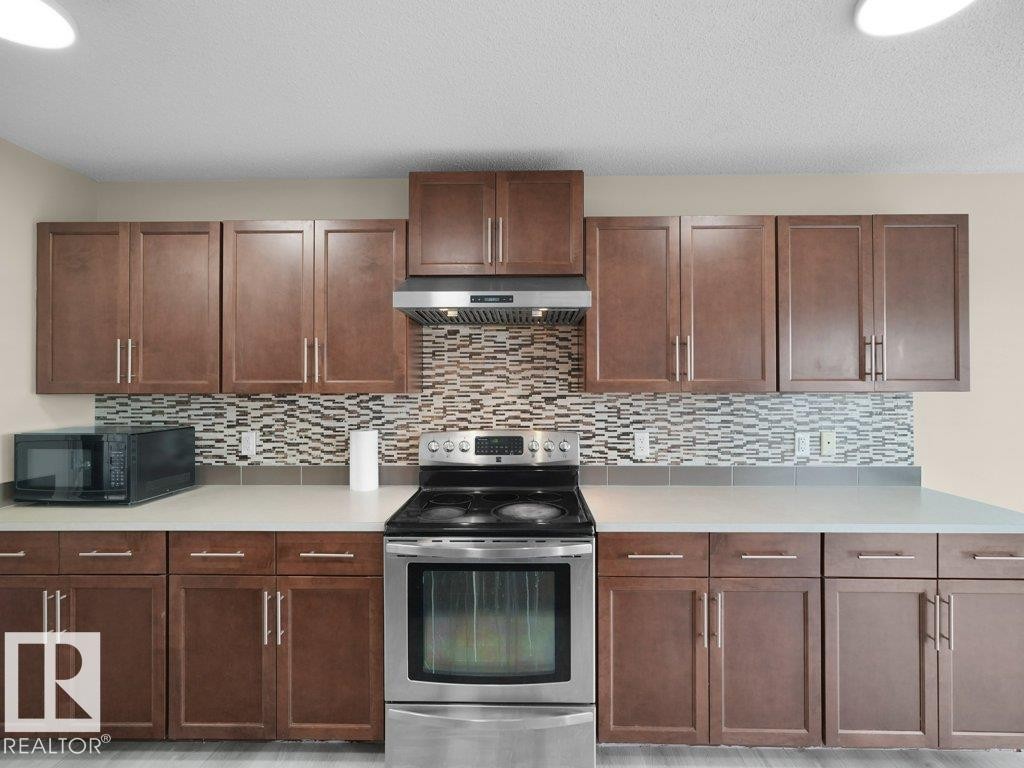 Stainless steel range with coordinating hood, extensive brown wood-finish cabinetry, light-toned countertops, and a patterned tile backsplash - 3010 17A Ave Nw, Edmonton, AB - Indoor Photo Showing Kitchen