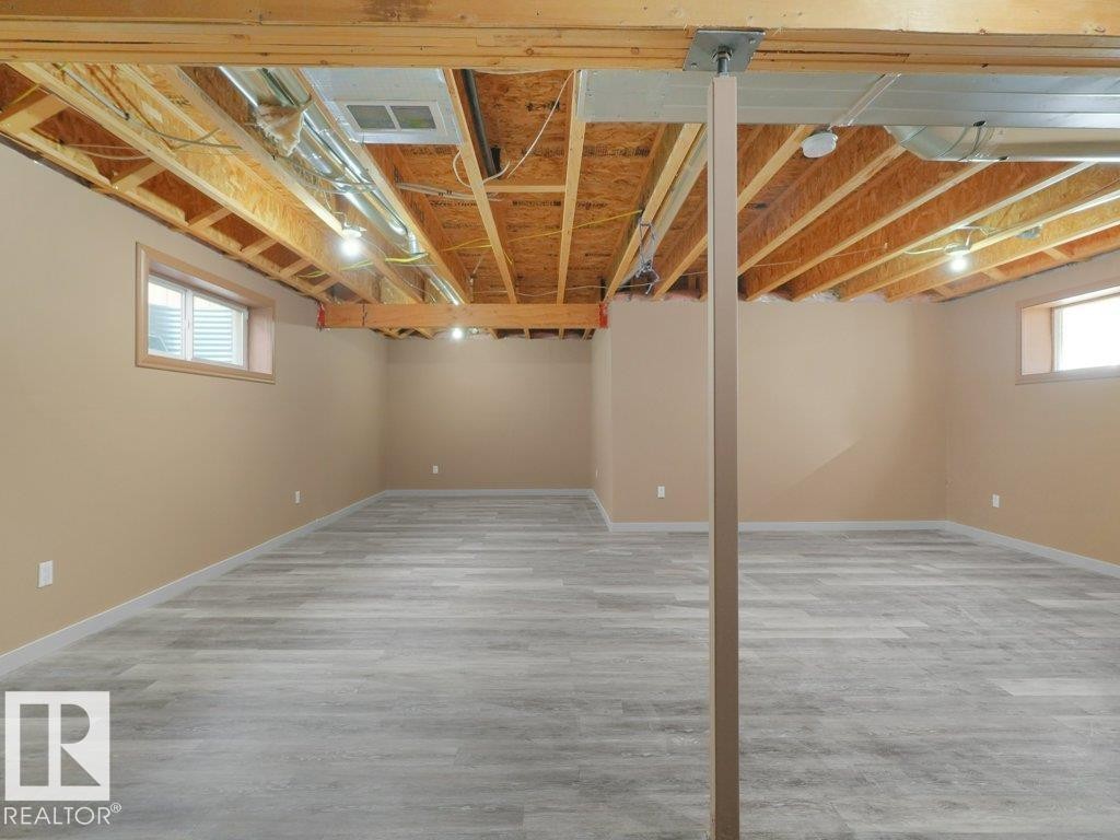 Finished lower level with wood-finish flooring, two windows, and exposed ceiling joists - 3010 17A Ave Nw, Edmonton, AB - Indoor Photo Showing Basement