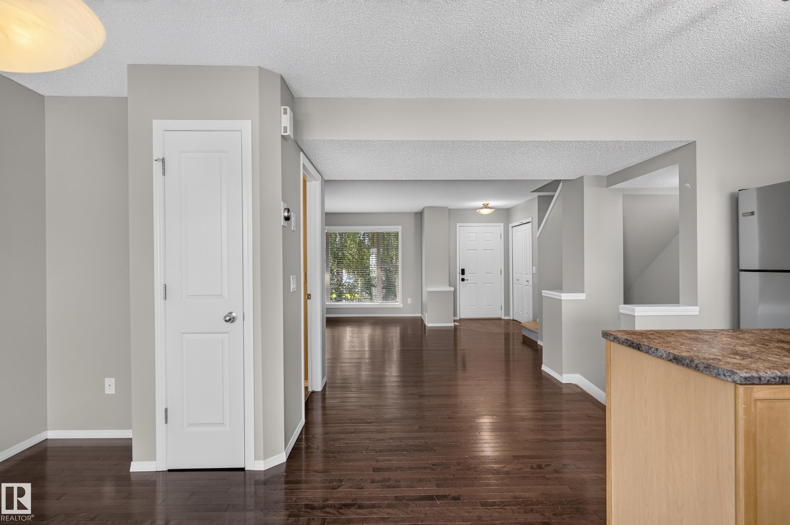 Hardwood-finish flooring, light gray wall paint, white trim, recessed lighting, and a partial kitchen counter with a stone-finish surface - 6008 South Terwillegar Boulevard Nw, Edmonton, AB - Indoor Photo Showing Other Room