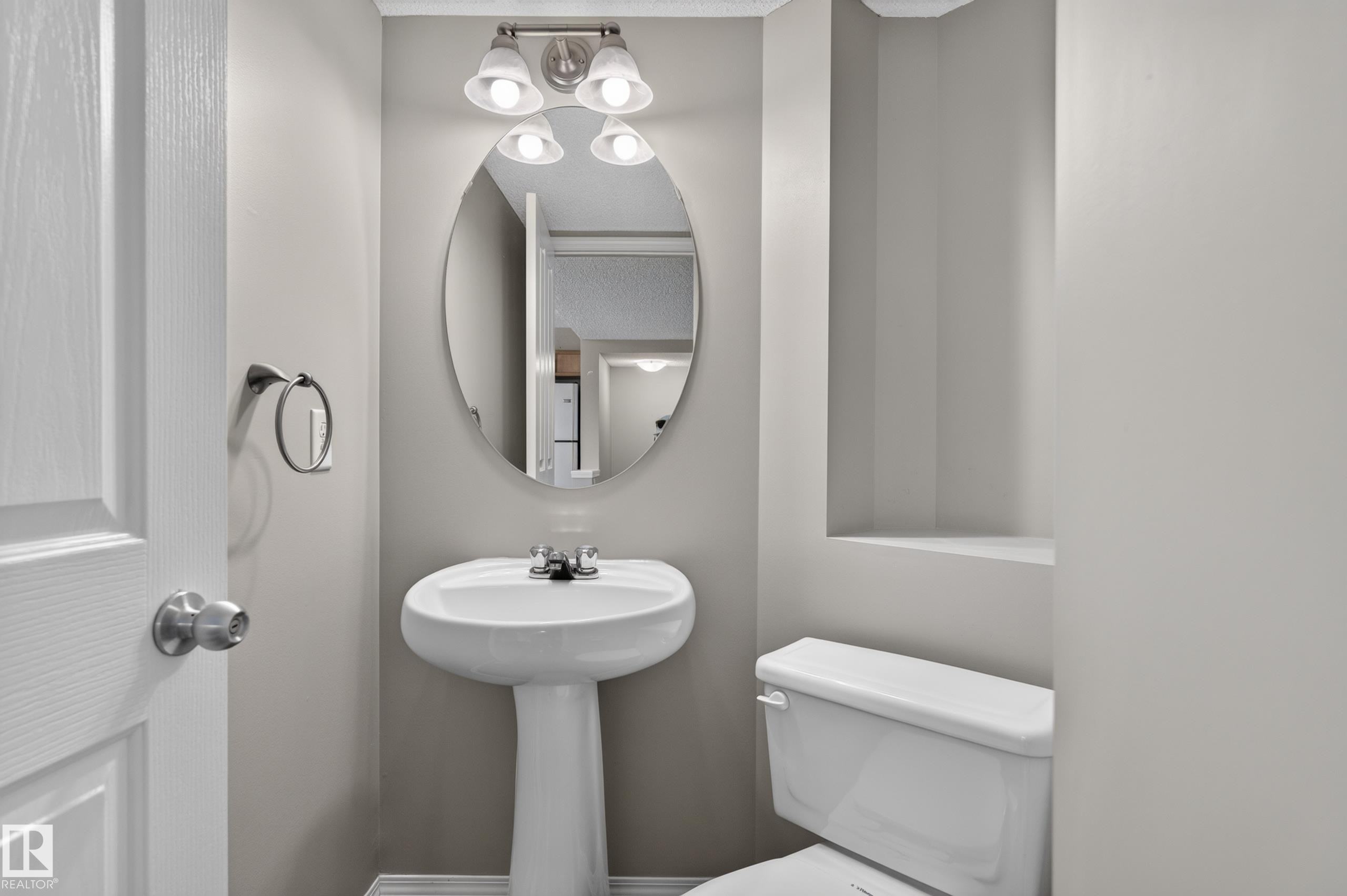 Pedestal sink with chrome faucet, oval mirror, and wall-mounted vanity lighting - 6008 South Terwillegar Boulevard Nw, Edmonton, AB - Indoor Photo Showing Bathroom