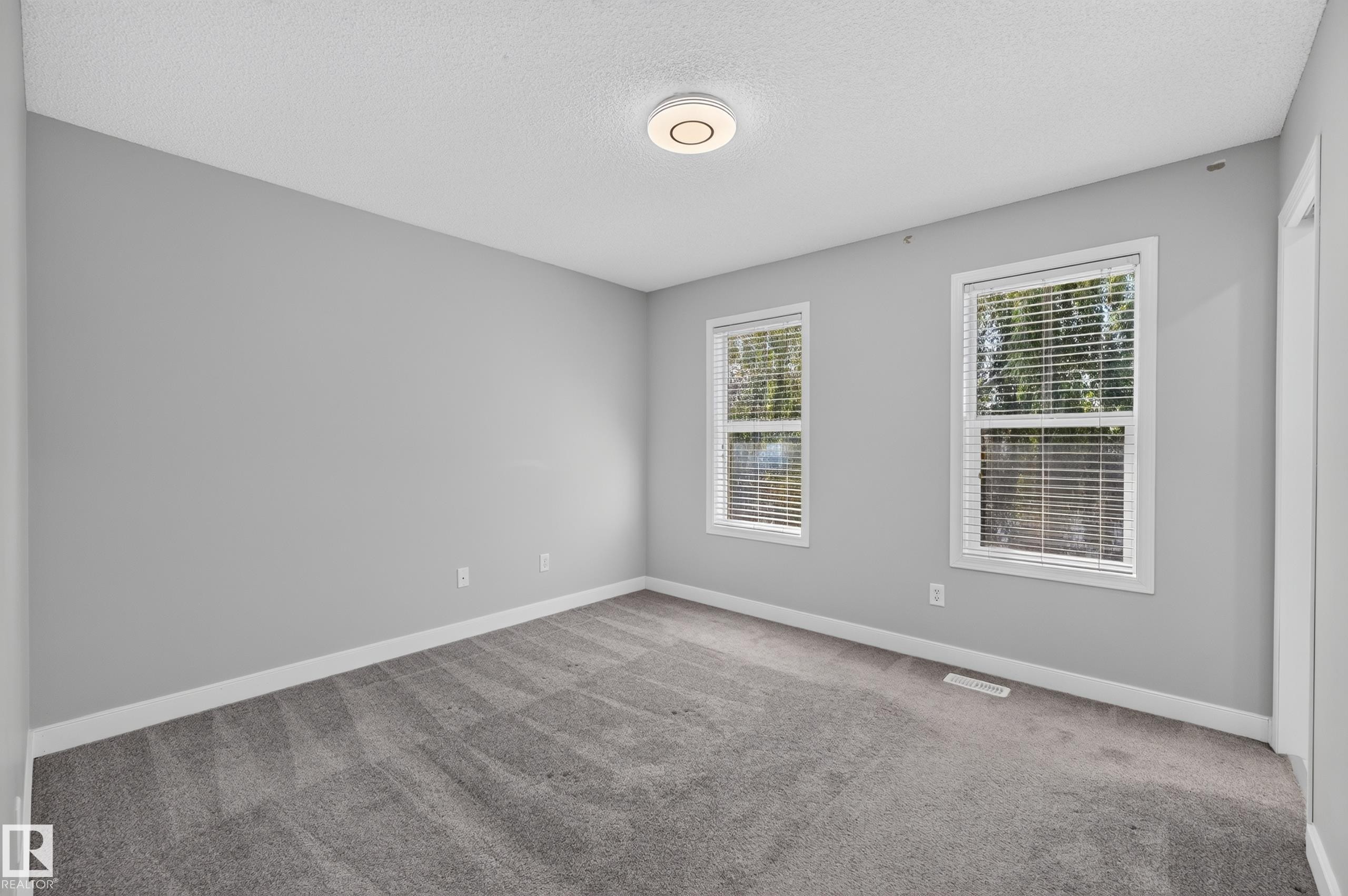Spacious room featuring neutral grey wall paint, plush grey carpeting, two windows with white blinds, and a modern circular flush-mount ceiling light - 6008 South Terwillegar Boulevard Nw, Edmonton, AB - Indoor Photo Showing Other Room
