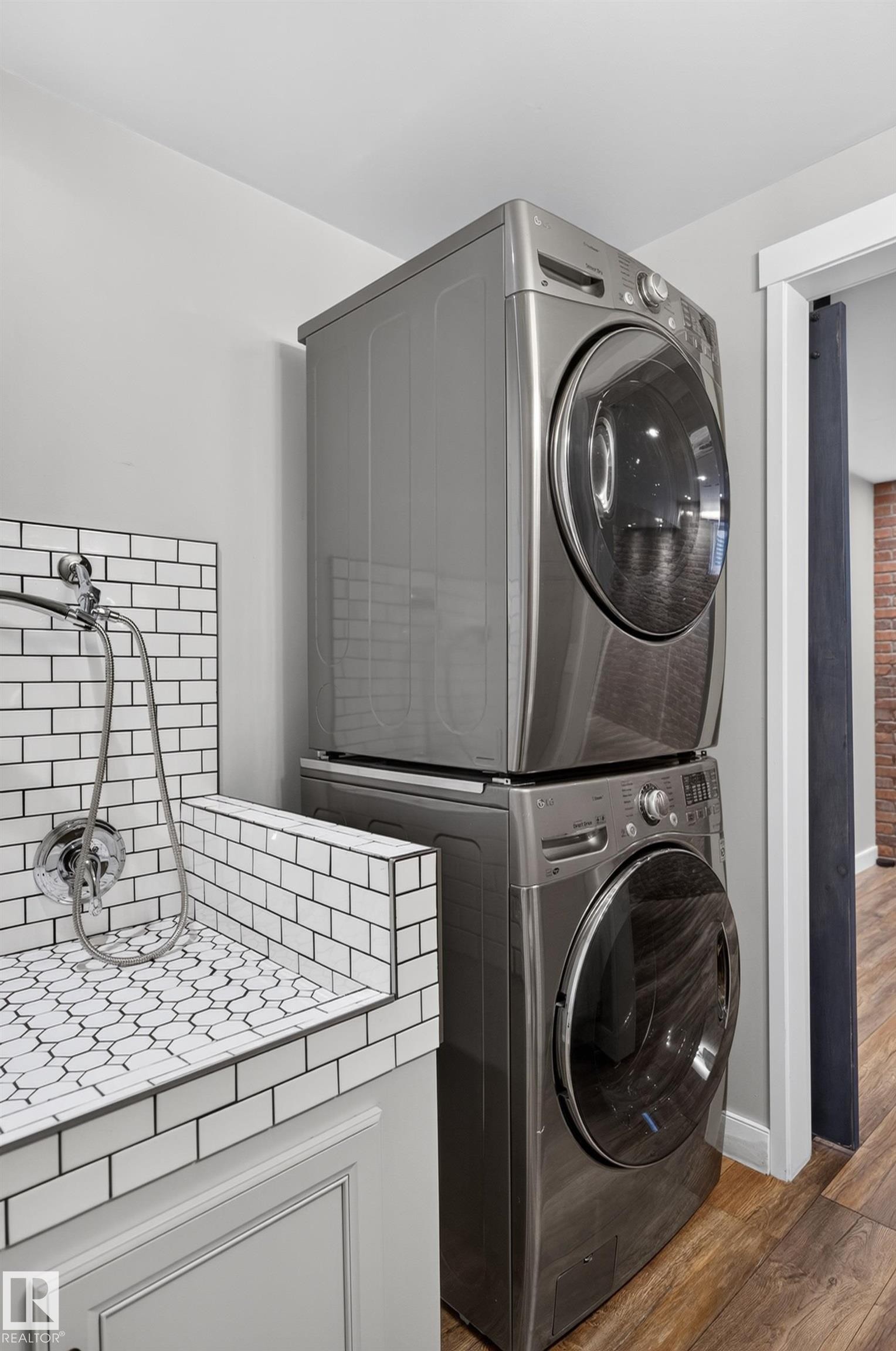 Stacked laundry appliances, white subway tile surround, patterned tile basin, chrome fixtures, wood-finish flooring - 6008 South Terwillegar Boulevard Nw, Edmonton, AB - Indoor Photo Showing Laundry Room