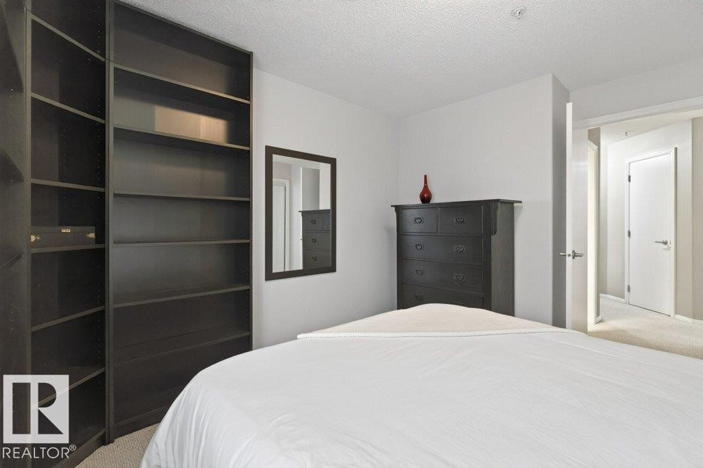 Built-in shelving unit, neutral wall color, and light-toned carpet - #201 10528 77 Av Nw, Edmonton, AB - Indoor Photo Showing Bedroom