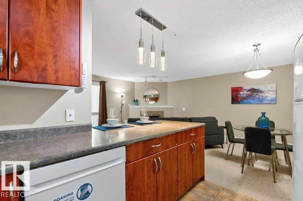 Kitchen island with integrated dishwasher, wood-finish cabinetry, and contemporary pendant lighting - #201 10528 77 Av Nw, Edmonton, AB - Indoor Photo Showing Kitchen