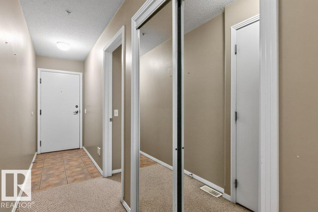 Entryway featuring durable tile flooring, plush carpeting, a flush-mount ceiling light, and mirrored closet doors - #201 10528 77 Av Nw, Edmonton, AB - Indoor Photo Showing Other Room
