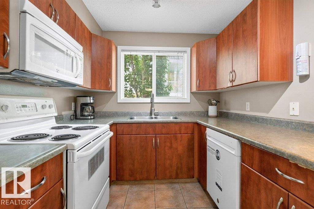 U-shaped kitchen with wood-finish cabinetry, a window with blinds, and tile flooring - #201 10528 77 Av Nw, Edmonton, AB - Indoor Photo Showing Kitchen With Double Sink