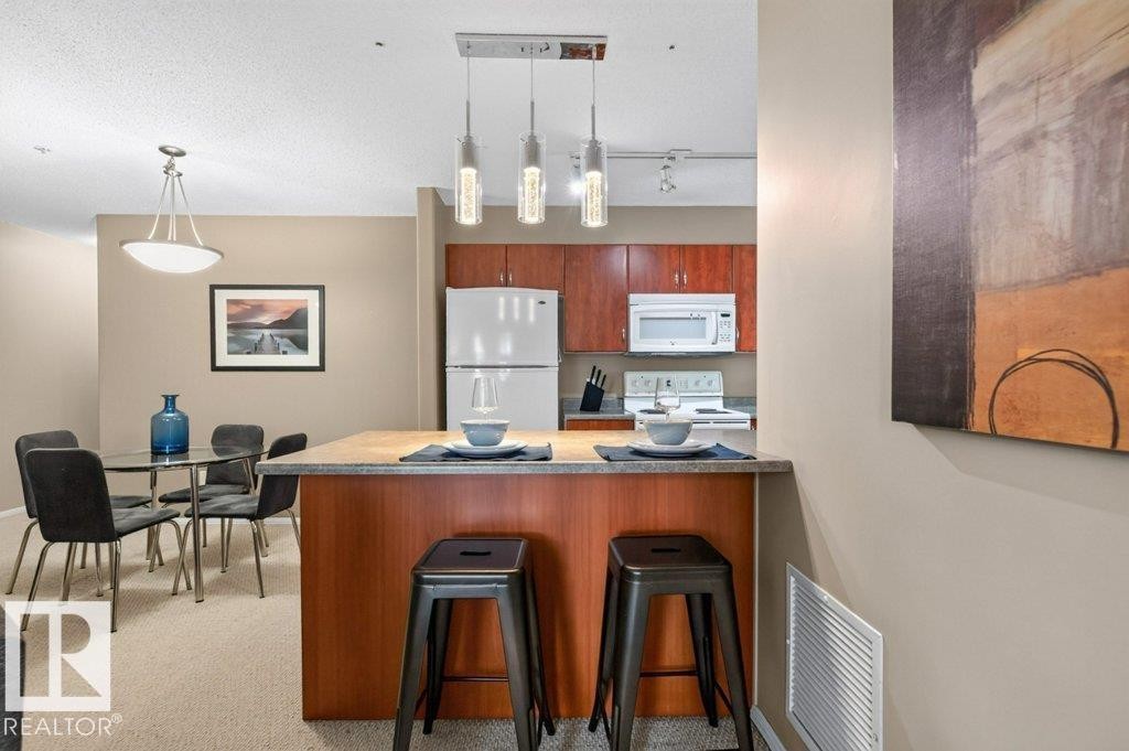 Kitchenette with wood-finish cabinetry, white appliances, and a breakfast bar with a wood-finish countertop - #201 10528 77 Av Nw, Edmonton, AB - Indoor Photo Showing Kitchen