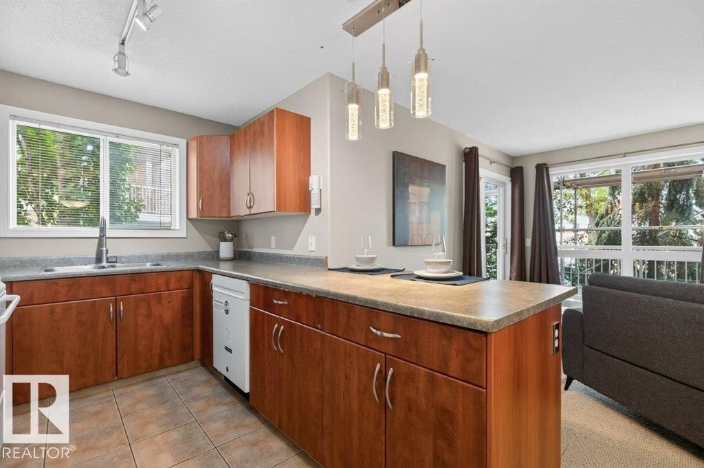 Contemporary kitchen featuring rich wood cabinetry with stainless steel hardware, quartz countertops, and a generously proportioned island with seating - #201 10528 77 Av Nw, Edmonton, AB - Indoor Photo Showing Kitchen With Double Sink