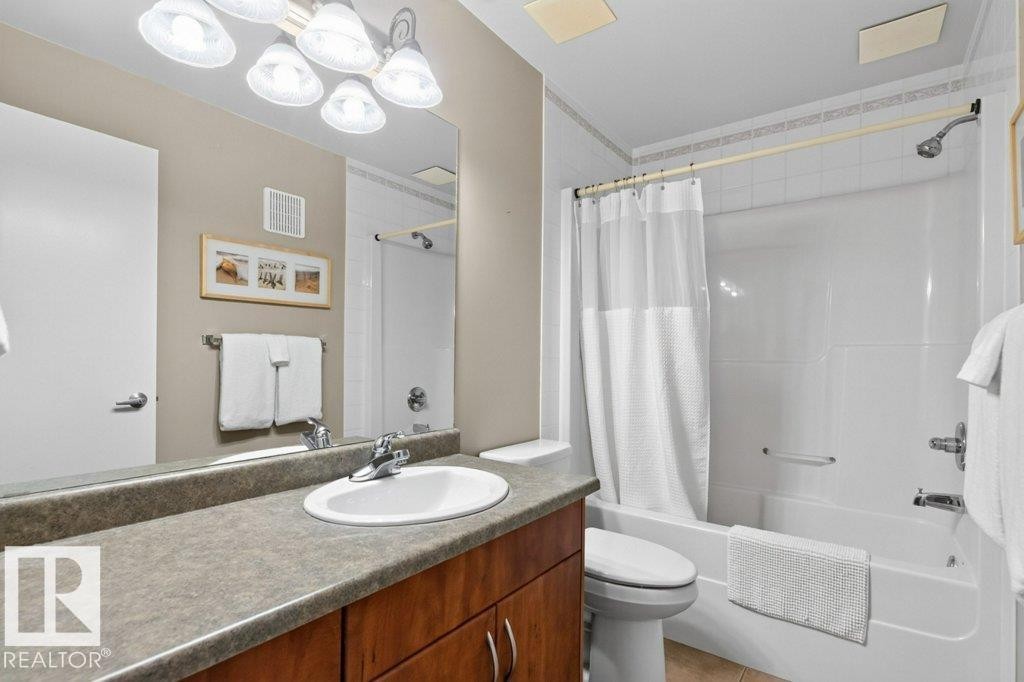 Bathroom featuring a vanity with a surface-mounted sink, wood-finish cabinetry, a large mirror, and a built-in bathtub with shower - #201 10528 77 Av Nw, Edmonton, AB - Indoor Photo Showing Bathroom