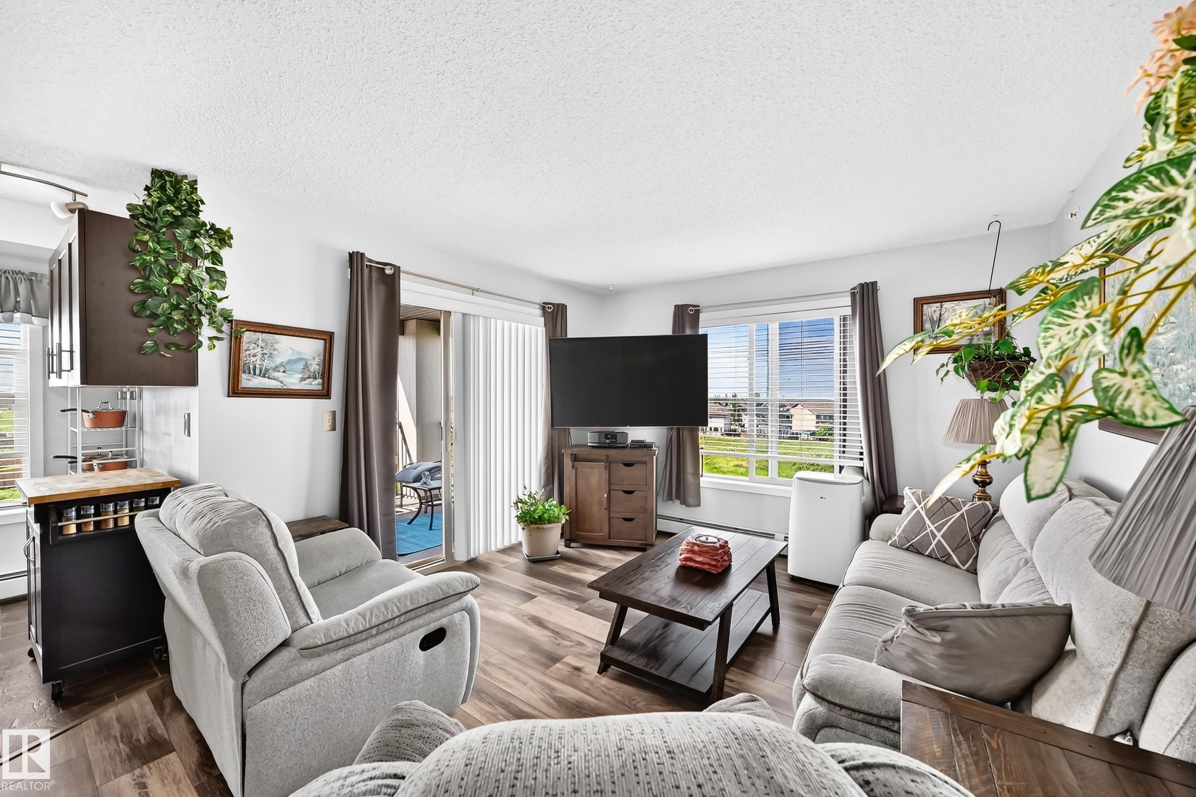 Wood-finish flooring throughout, bright white walls, and a sliding glass door providing outdoor access - #401 5390 Chappelle Rd Sw, Edmonton, AB