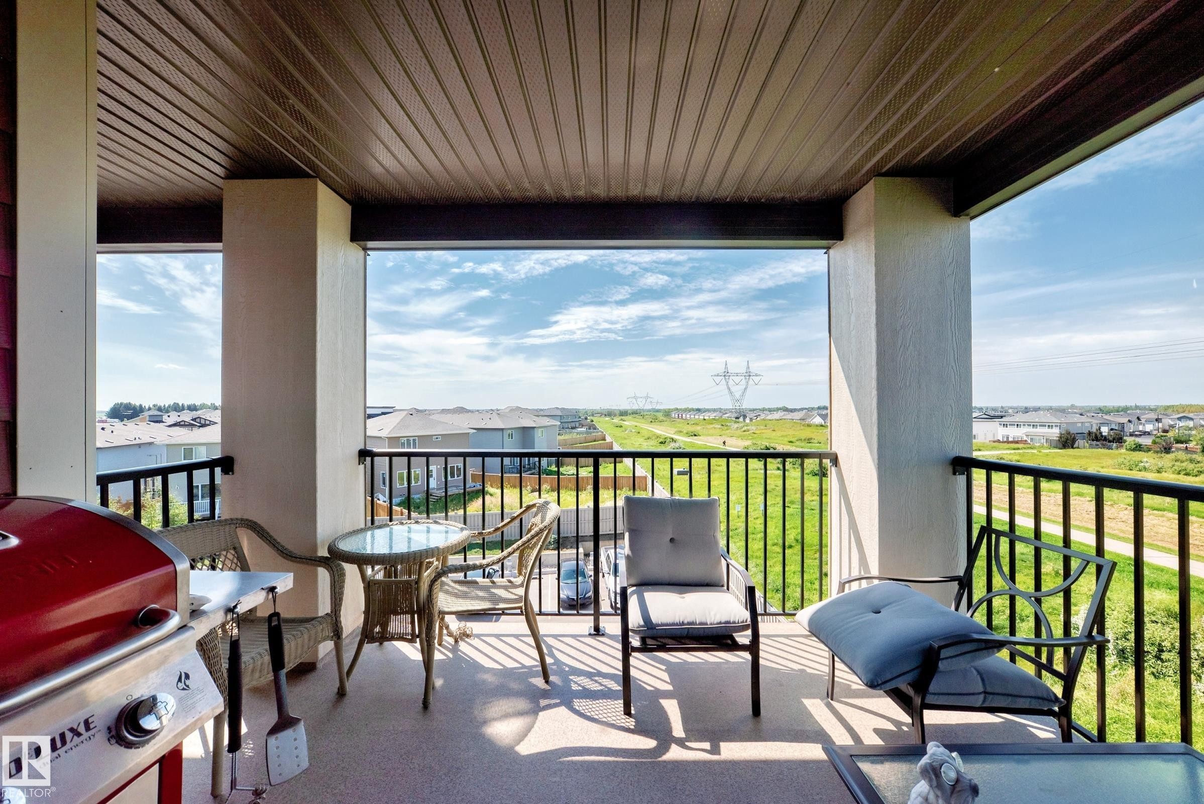 Covered balcony featuring a slatted ceiling, sturdy columns, and black metal railings - #401 5390 Chappelle Rd Sw, Edmonton, AB