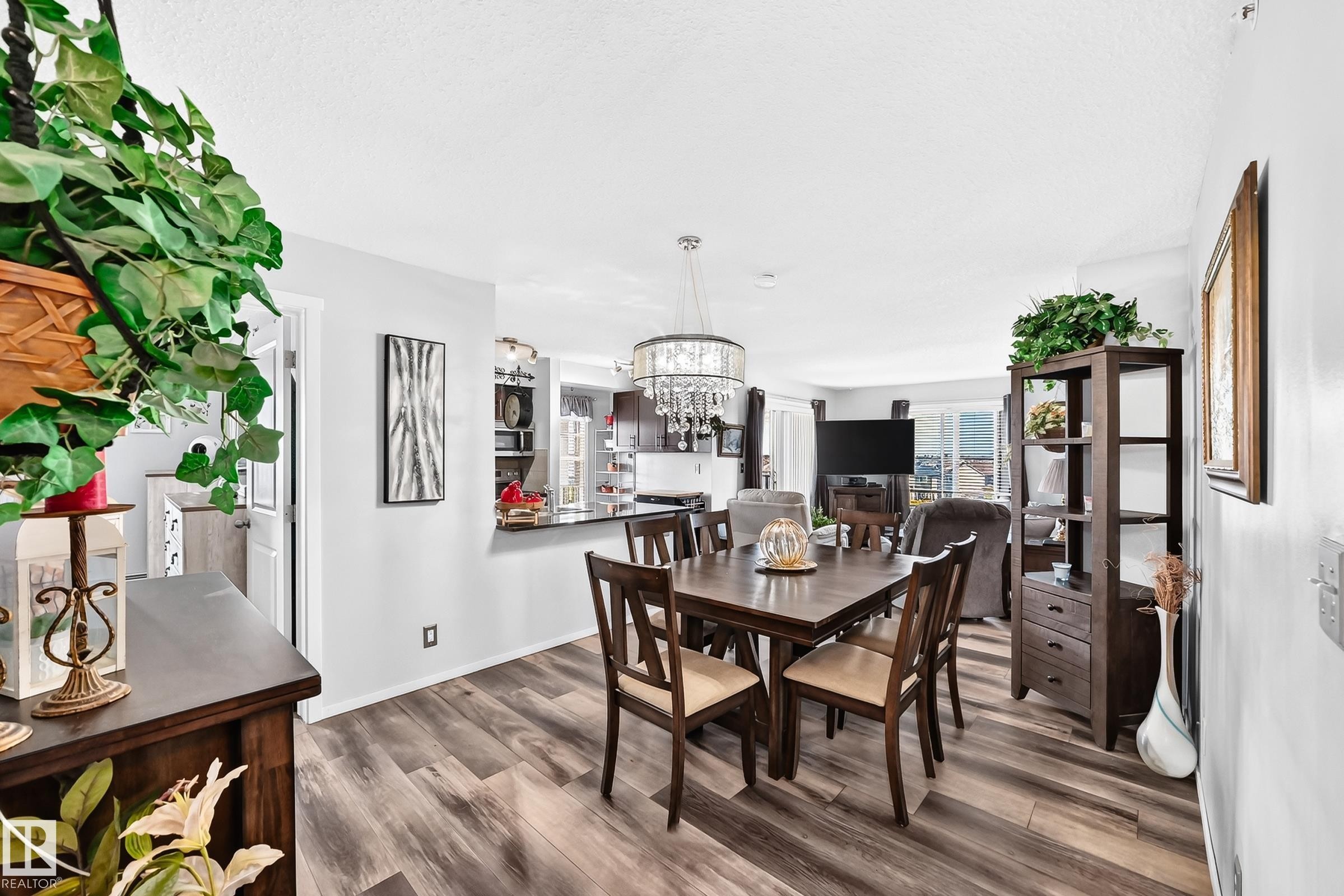 Wood-finish flooring throughout, with a crystal chandelier, and a black countertop bar - #401 5390 Chappelle Rd Sw, Edmonton, AB