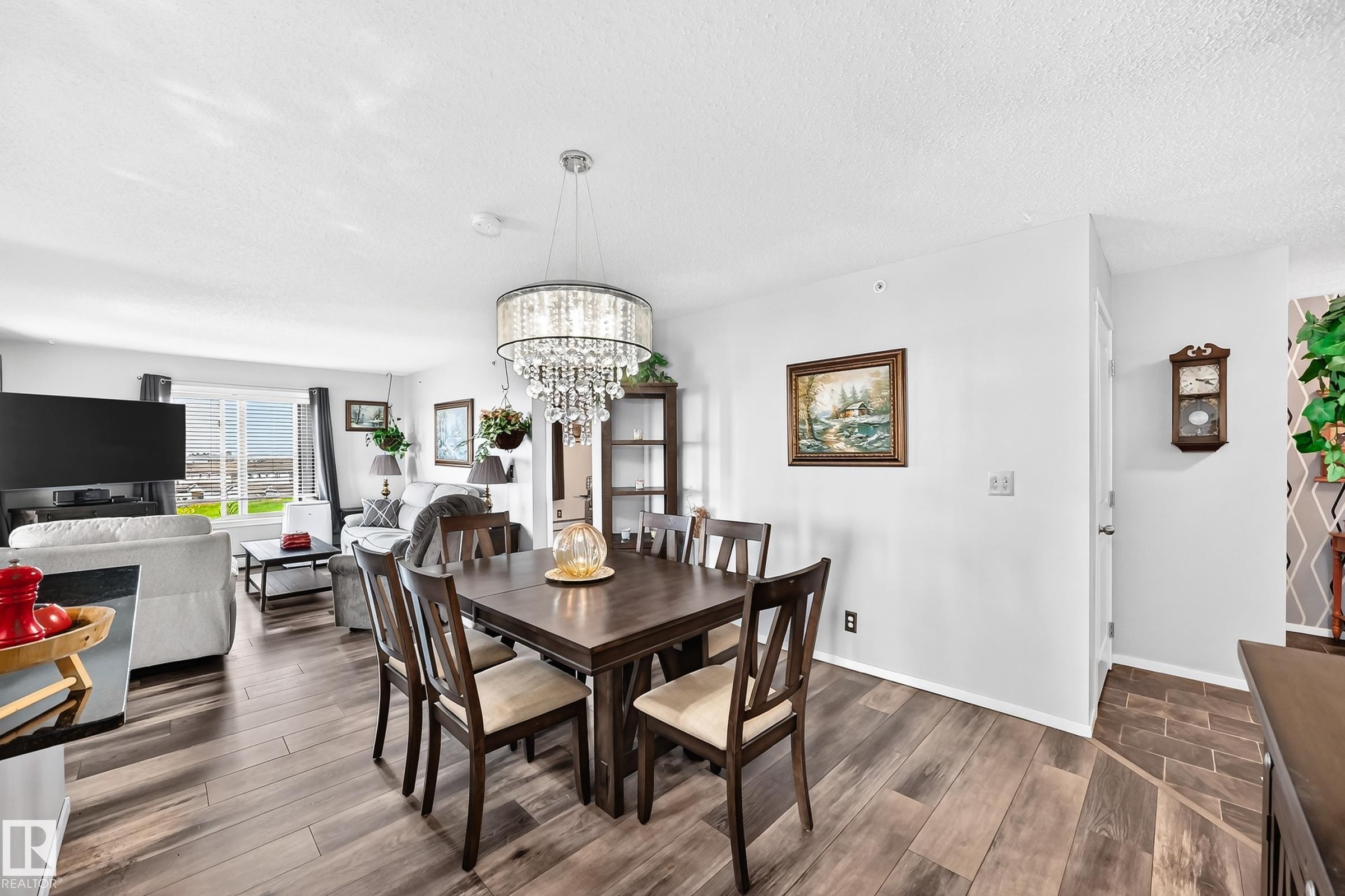 Hardwood-finish flooring throughout, a modern chandelier with crystal accents, and a large window offering natural light - #401 5390 Chappelle Rd Sw, Edmonton, AB