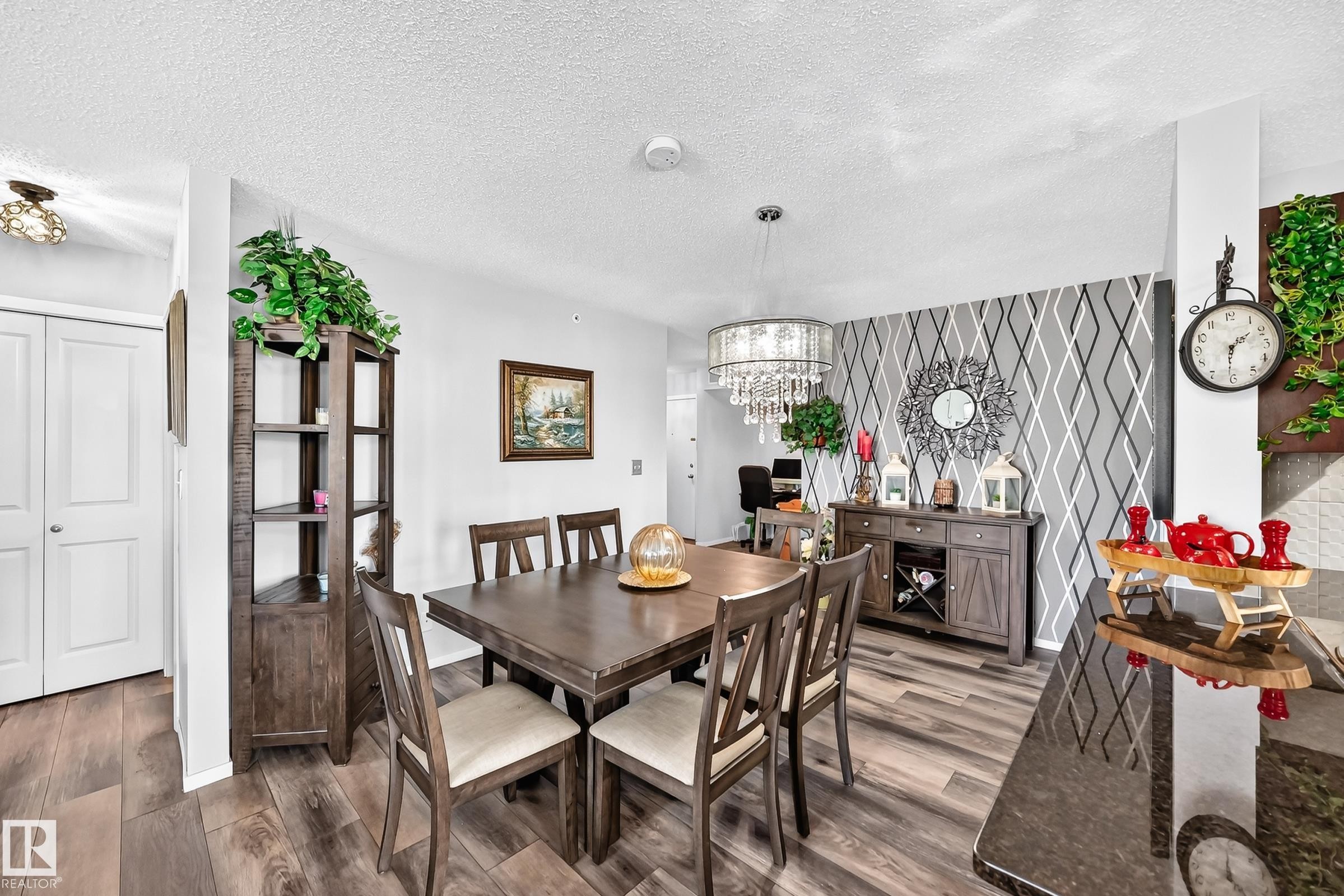Wood-finish flooring throughout, a geometric accent wall, and a crystal chandelier - #401 5390 Chappelle Rd Sw, Edmonton, AB