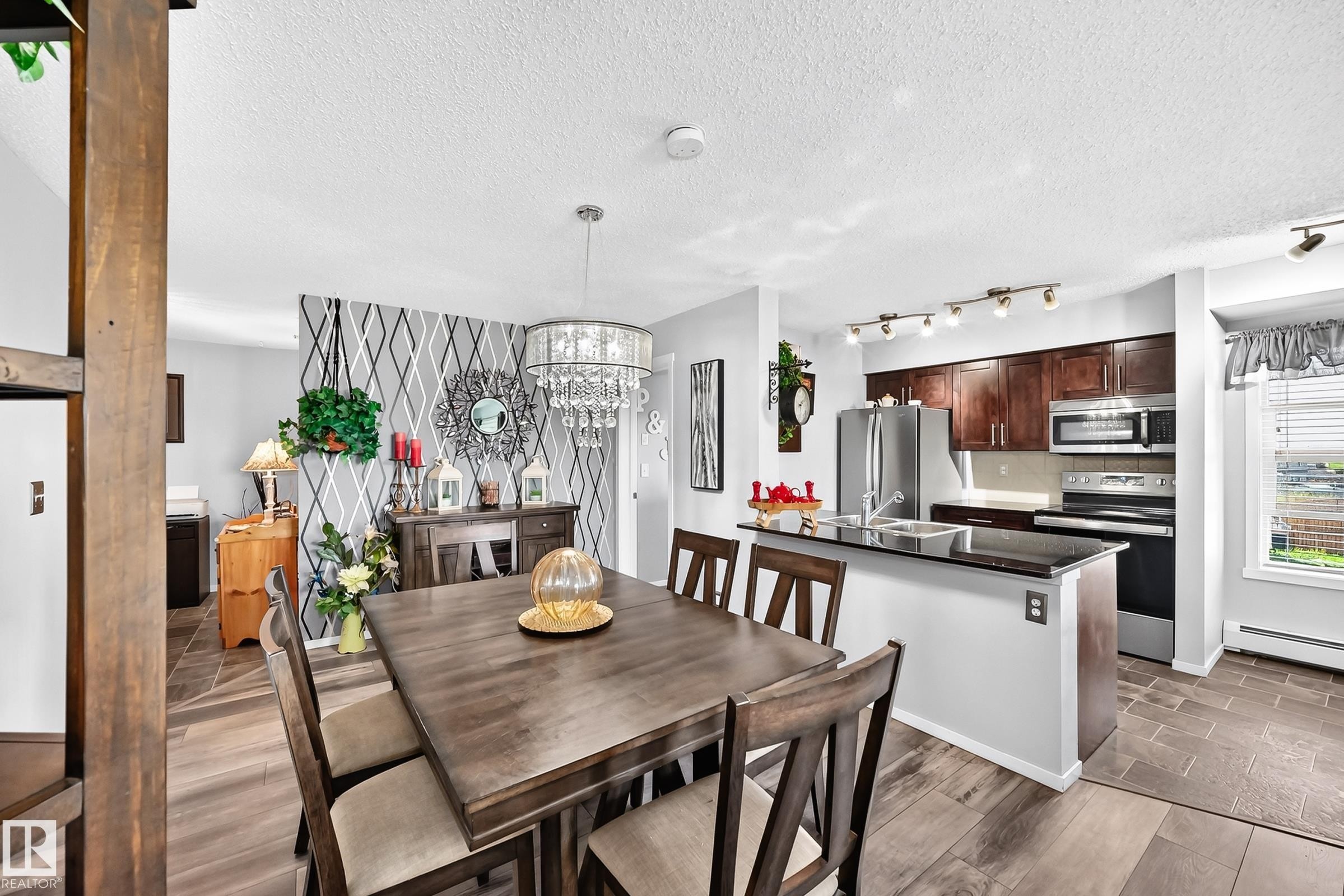 Modern kitchen featuring wood cabinetry, stainless steel appliances, and a black countertop - #401 5390 Chappelle Rd Sw, Edmonton, AB
