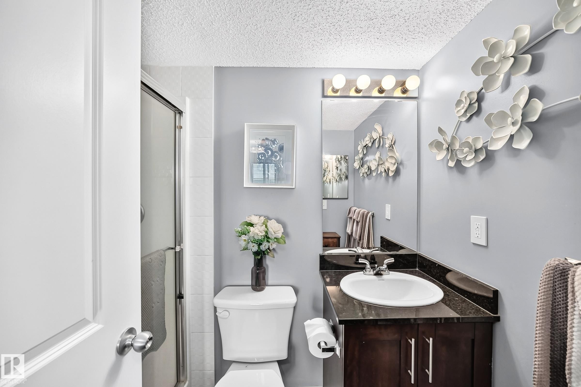Enclosed shower with a glass door, vanity with an integrated sink, dark countertop, and wood-finish cabinetry - #401 5390 Chappelle Rd Sw, Edmonton, AB