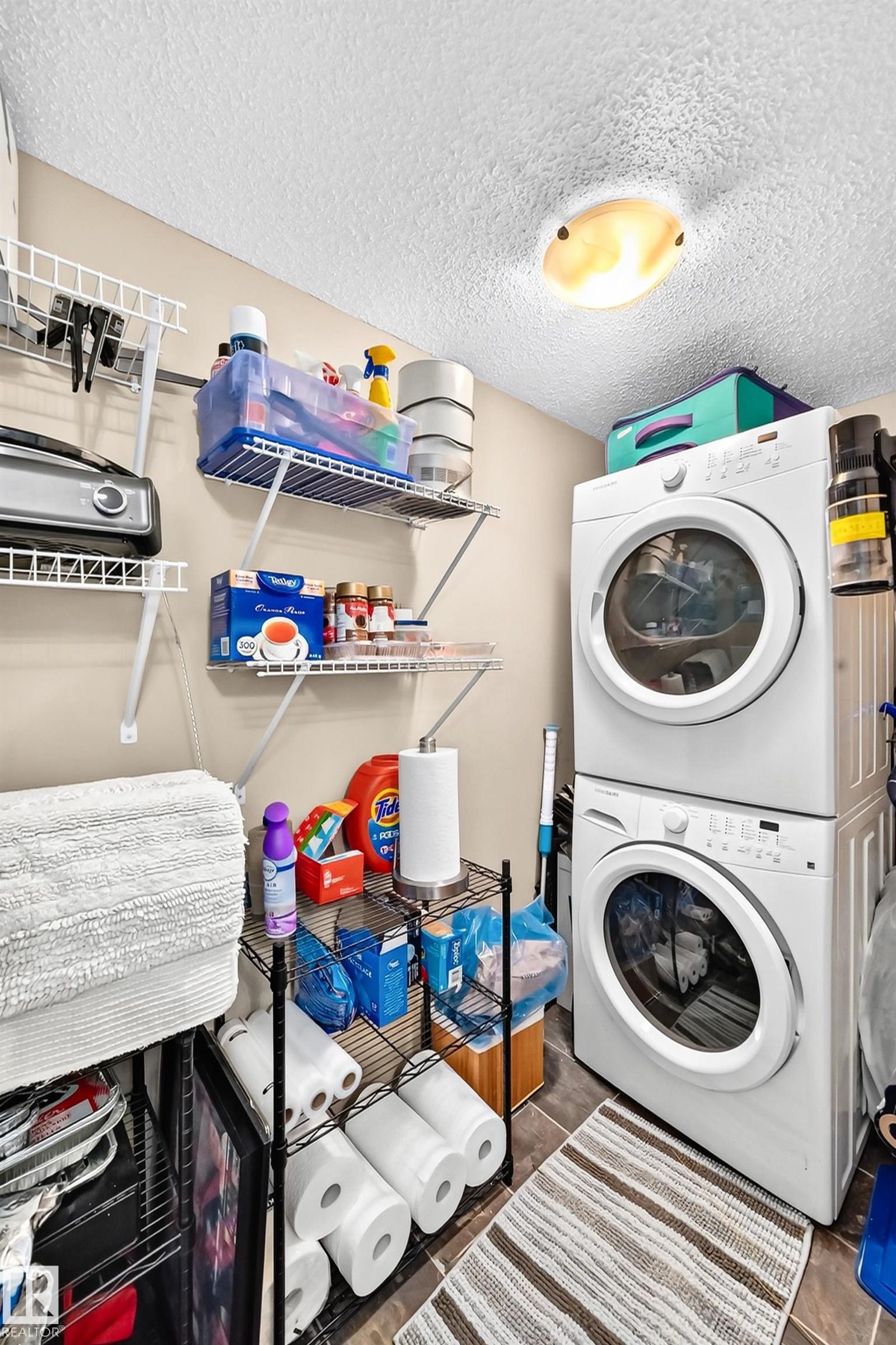 Stacked laundry appliances, wire shelving, and overhead lighting - #401 5390 Chappelle Rd Sw, Edmonton, AB