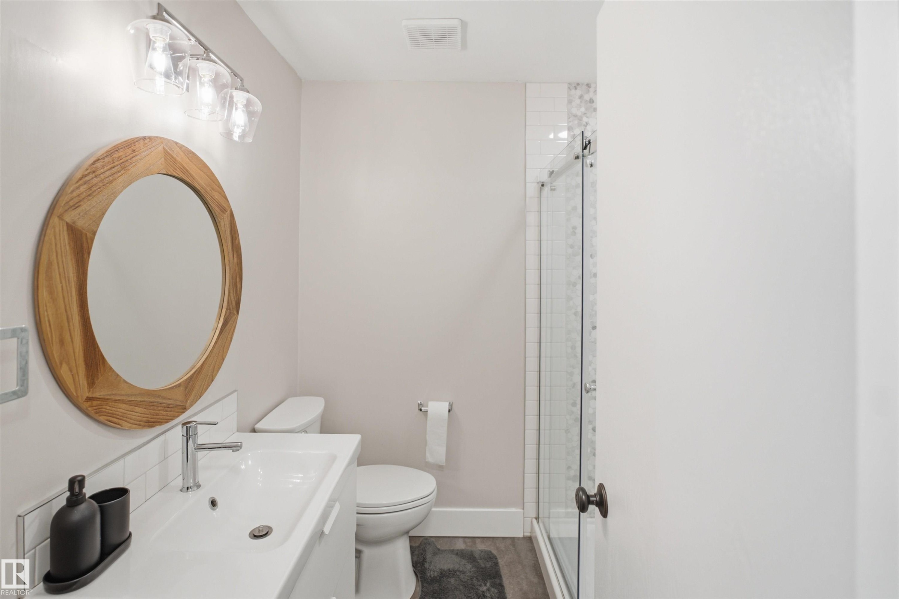 Wood-finish flooring, white vanity with integrated sink, chrome faucet, and a glass-enclosed shower with tile surround - 3515 20 Ave Nw, Edmonton, AB