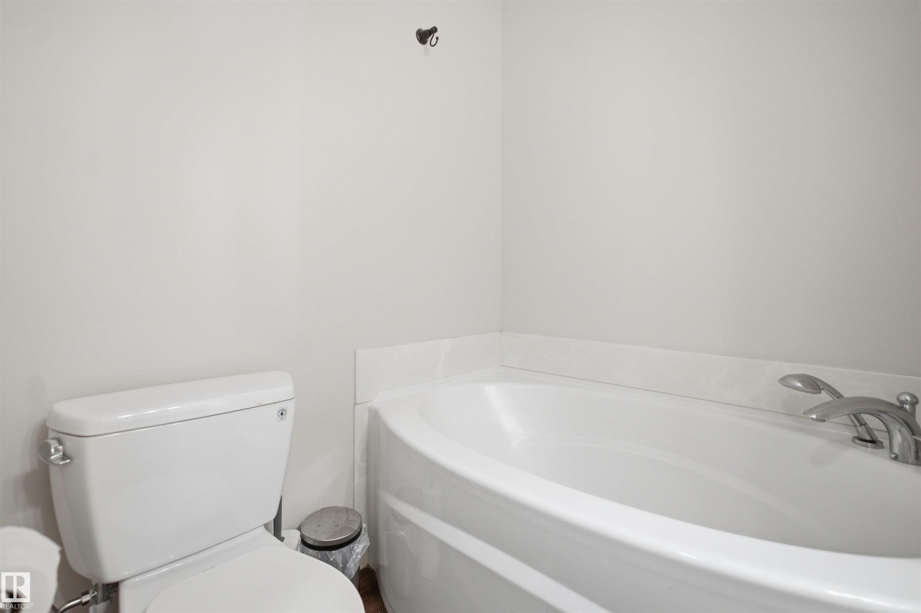 White built-in bathtub with deck-mounted chrome fixtures, white toilet, and light-colored walls - 3515 20 Ave Nw, Edmonton, AB