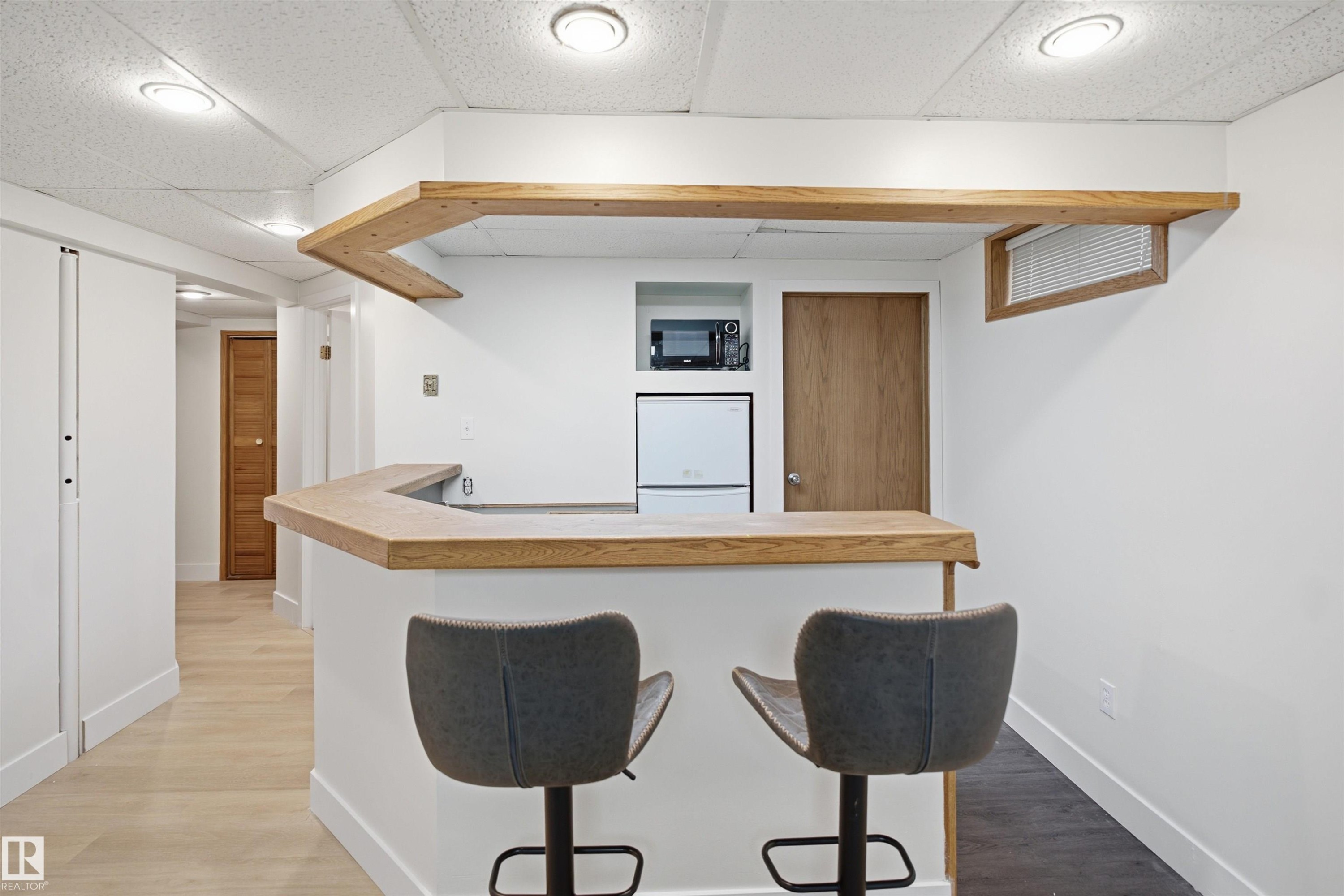Built-in bar with wood-finish countertop, recessed lighting, integrated microwave, compact refrigerator, and wood-finish flooring - 3515 20 Ave Nw, Edmonton, AB