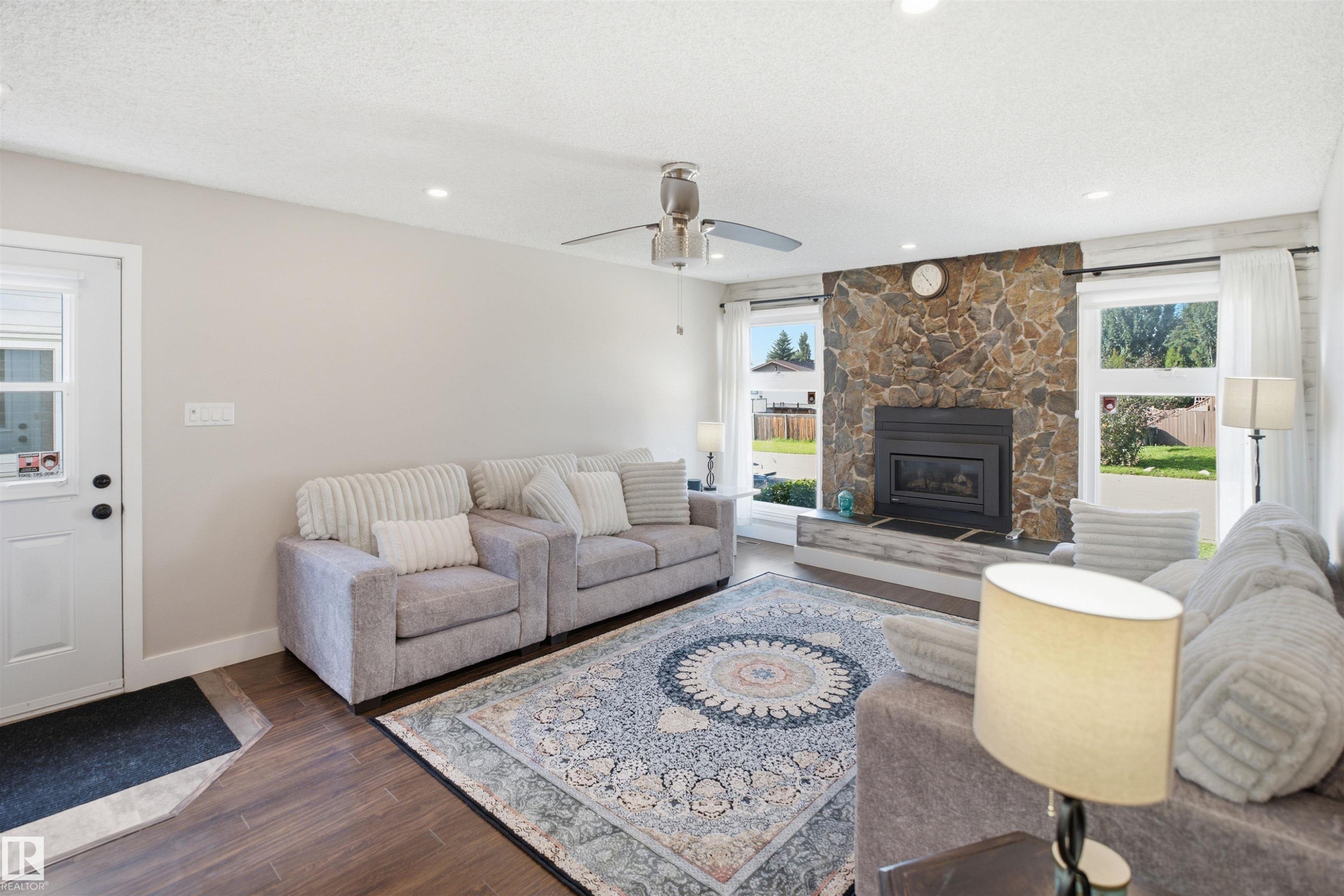Stone-faced fireplace with a built-in firebox, wood-finish flooring, recessed lighting, ceiling fan, and multiple windows with white trim - 3515 20 Ave Nw, Edmonton, AB