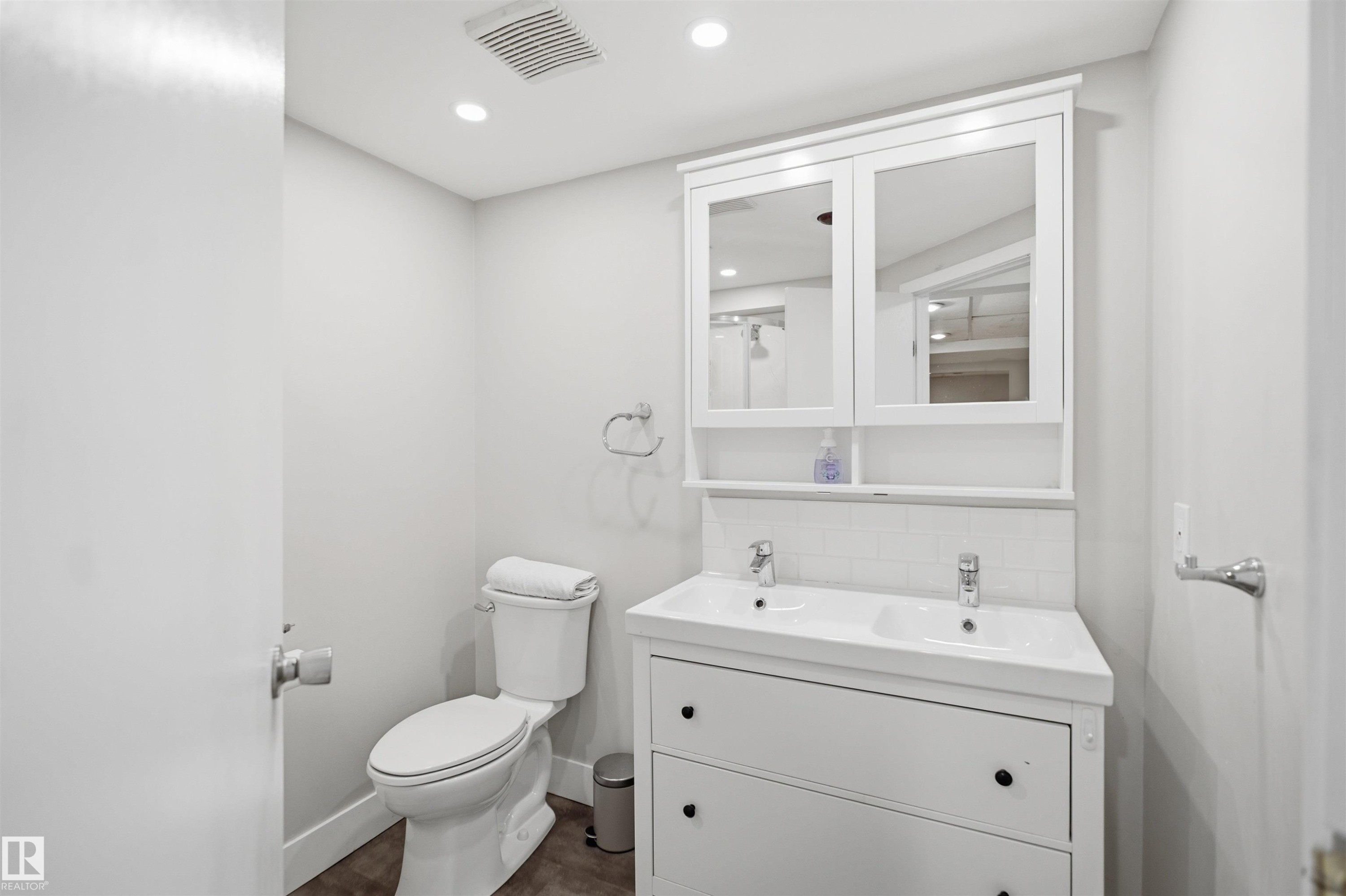 Dual-sink vanity with white cabinetry, tile backsplash, and mirrored medicine cabinet - 3515 20 Ave Nw, Edmonton, AB