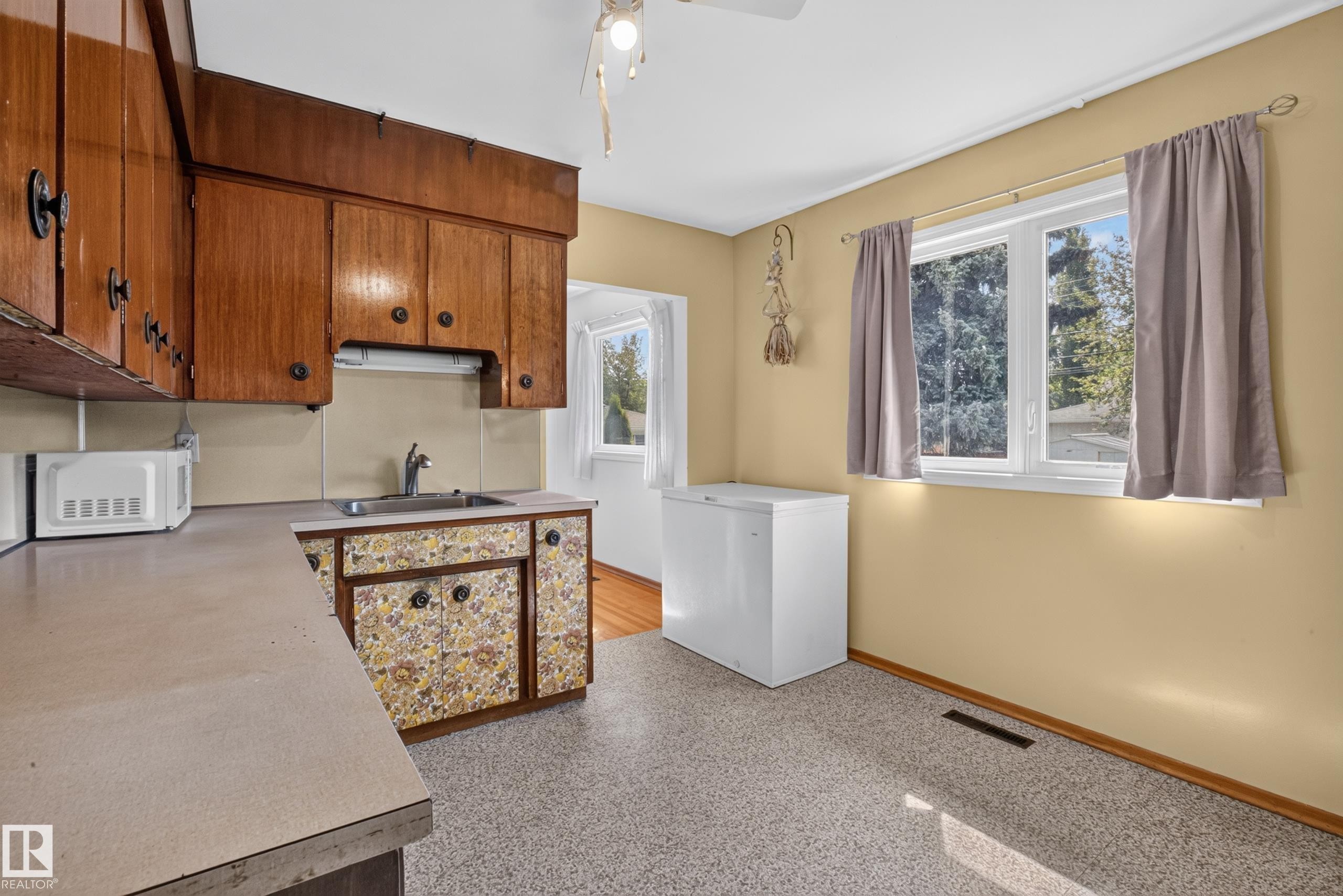Wood cabinetry, laminate countertops, stainless steel sink, large window, and light-toned flooring - 16009 93A Avenue Nw, Edmonton, AB - Indoor Photo Showing Kitchen
